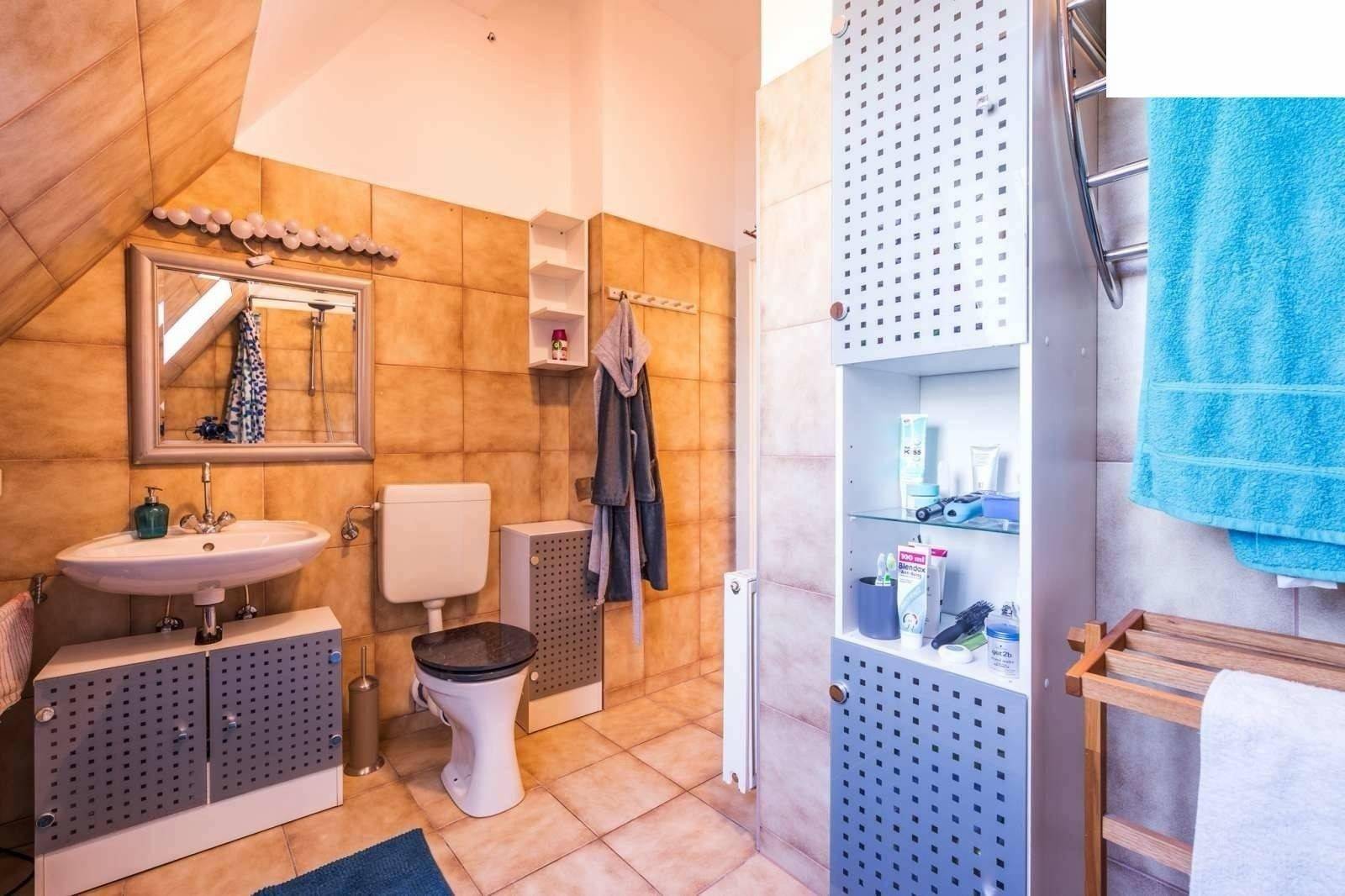 Badezimmer mit Waschbecken, Spiegel, Toilette und beigefarbenen Fliesen unter der Dachschräge.