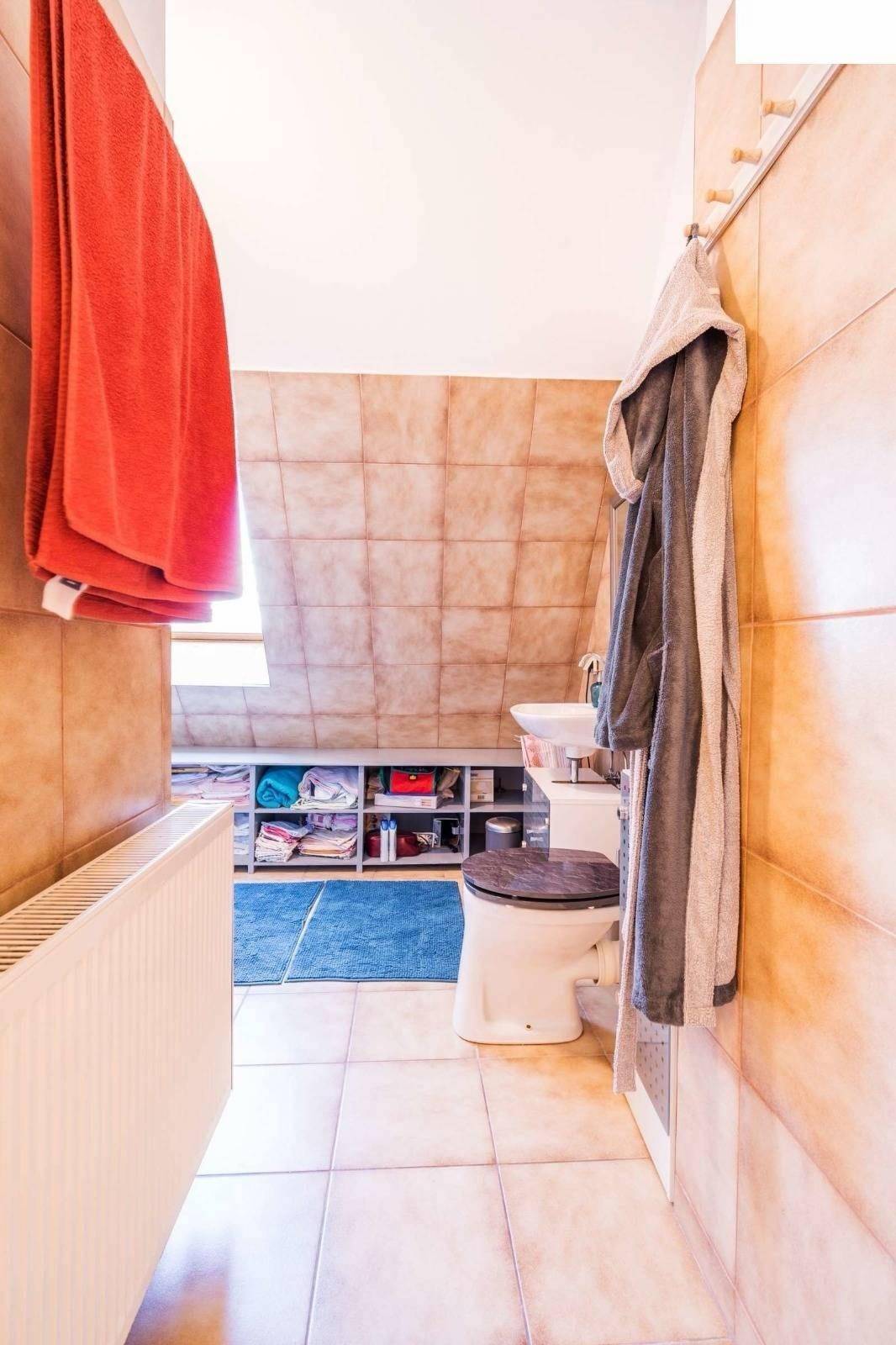 Badezimmer mit beigefarbenen Fliesen, Toilette und Dachschräge, funktional eingerichtet.