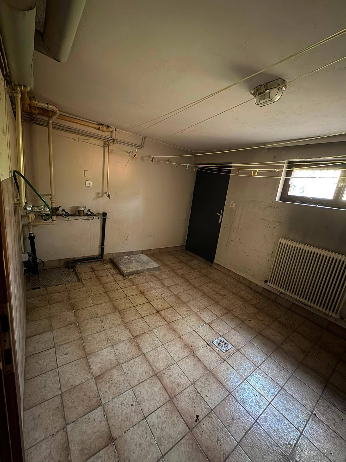 Hauswirtschaftsraum im Keller mit Fliesenboden, sichtbaren Rohren und Heizkörper.
