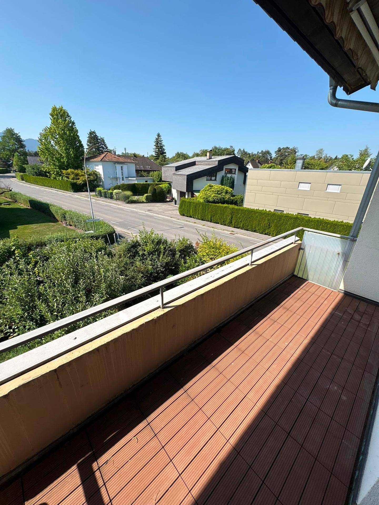Balkon mit Holzboden und Blick auf die Straße und die umliegende Wohngegend.