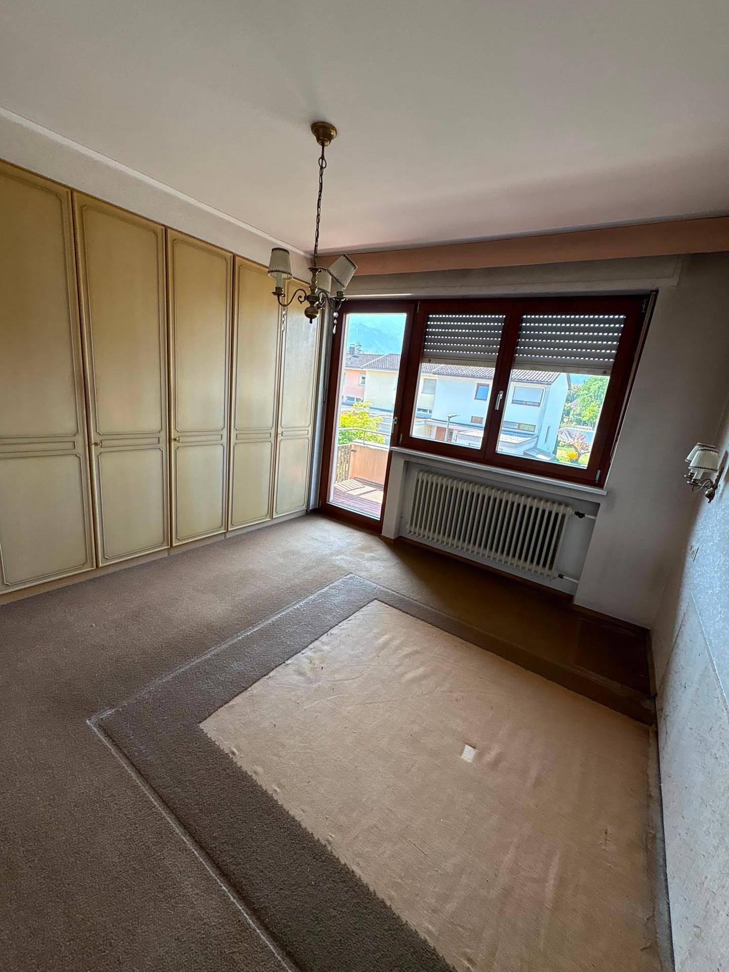 Helles Schlafzimmer mit Teppichboden, Einbauschrank und Fenster mit Blick ins Grüne.
