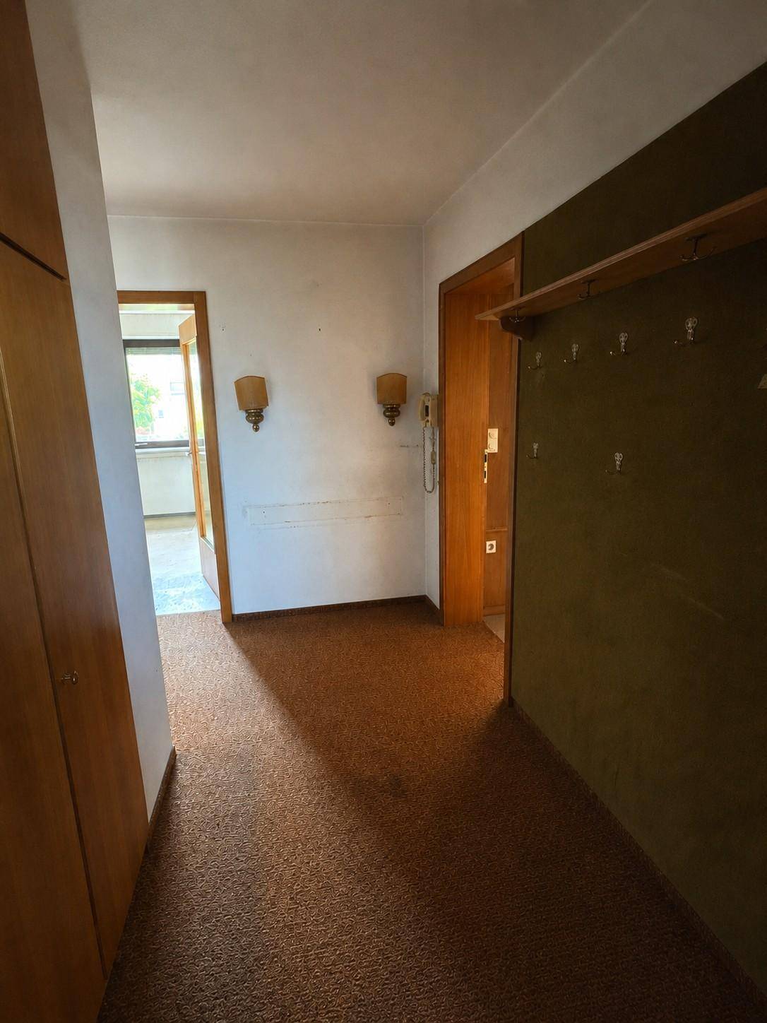 Flur mit Teppichboden, Einbauschrank aus Holz und Blick in einen weiteren Raum.