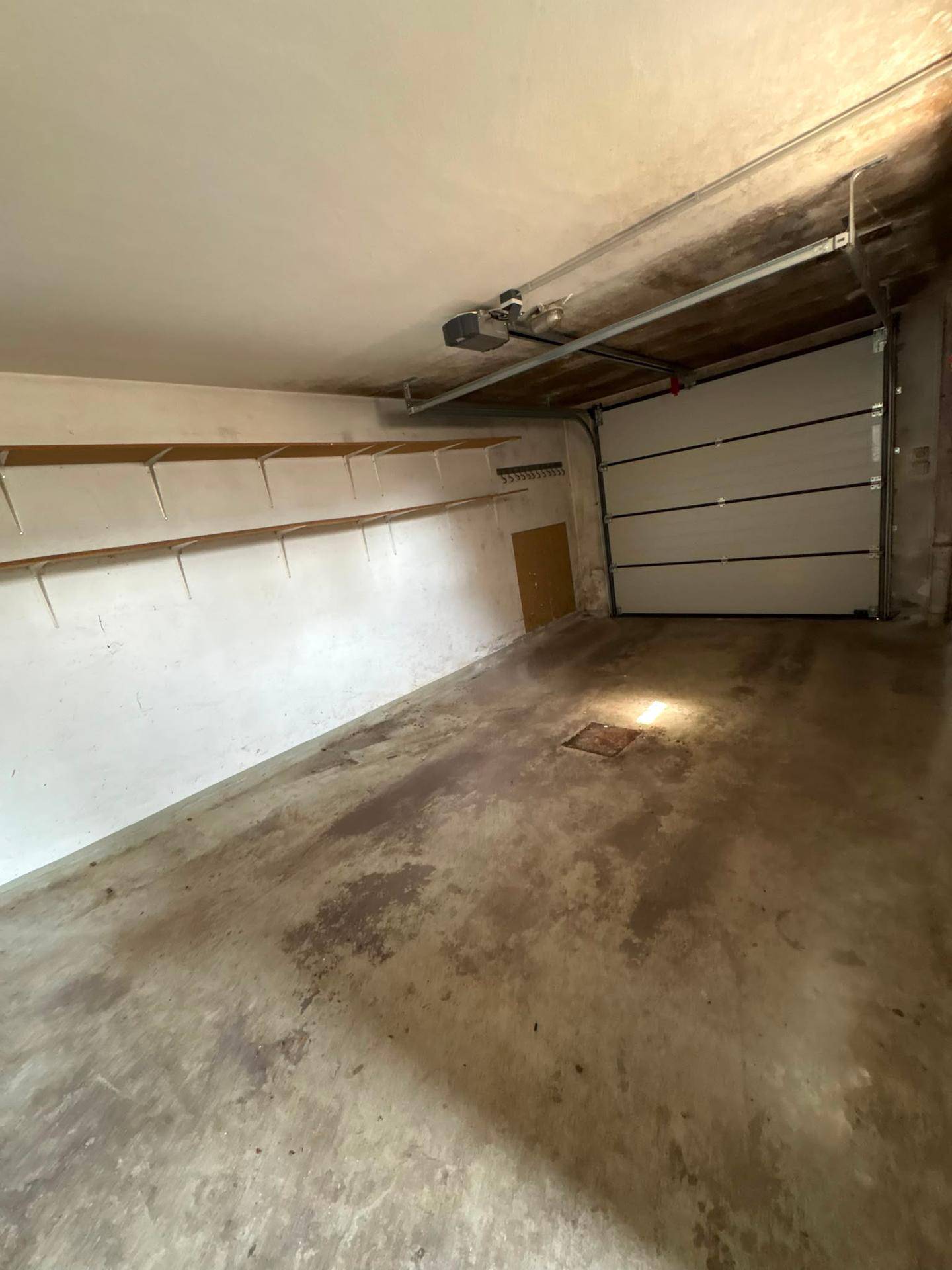 Leere Garage mit Betonboden, Regalen und einem automatischen Garagentor.