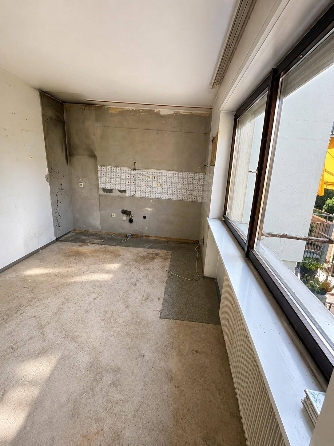 Leerer Raum, vermutlich eine Küche, mit freigelegten Wänden und großem Fenster.