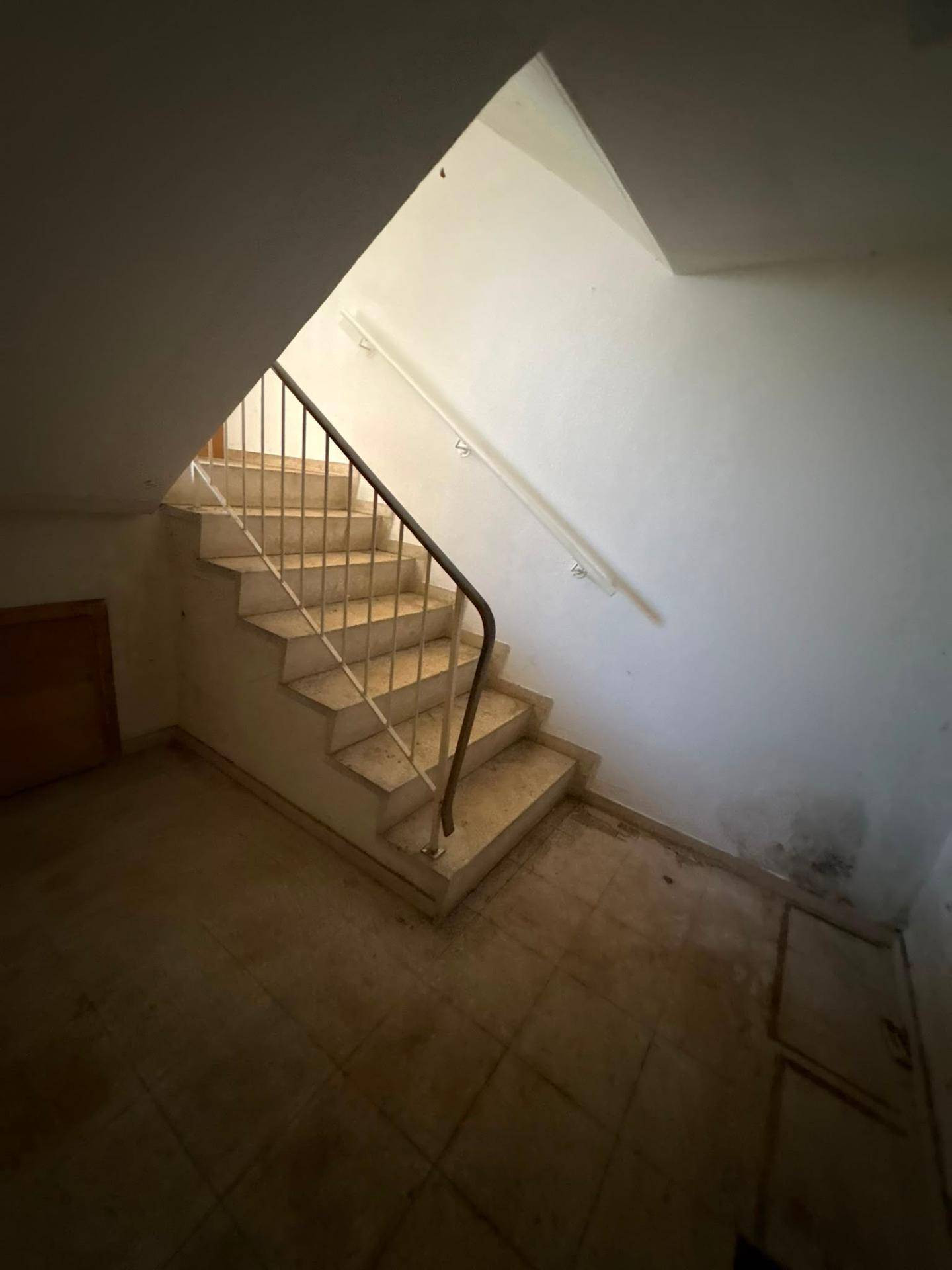 Treppenabgang in den Keller mit Fliesenboden und schlichtem Geländer.