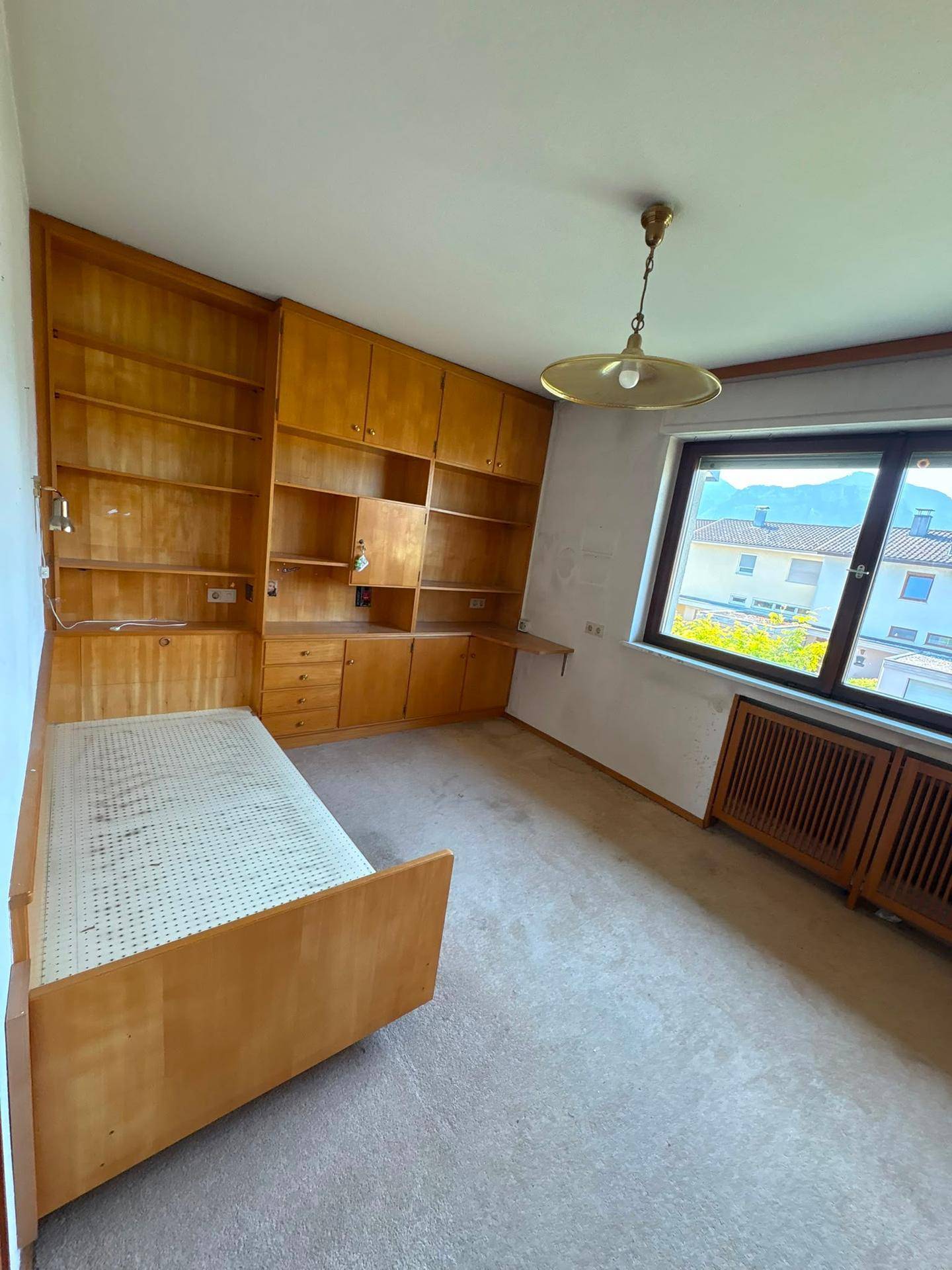 Schlafzimmer mit Teppichboden, eingebautem Holzregal und Einzelbett.