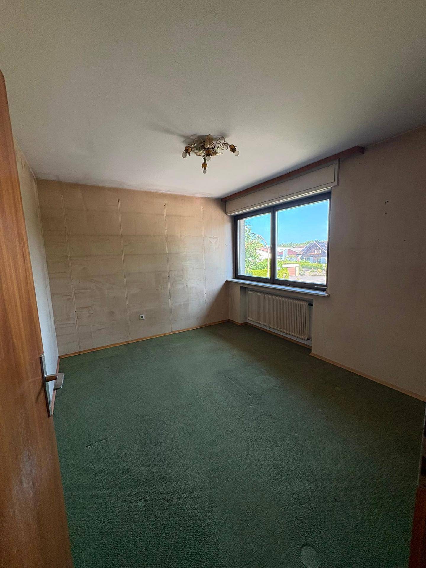 Schlafzimmer mit grünem Teppichboden, Fenster und ungestrichenen Wänden.