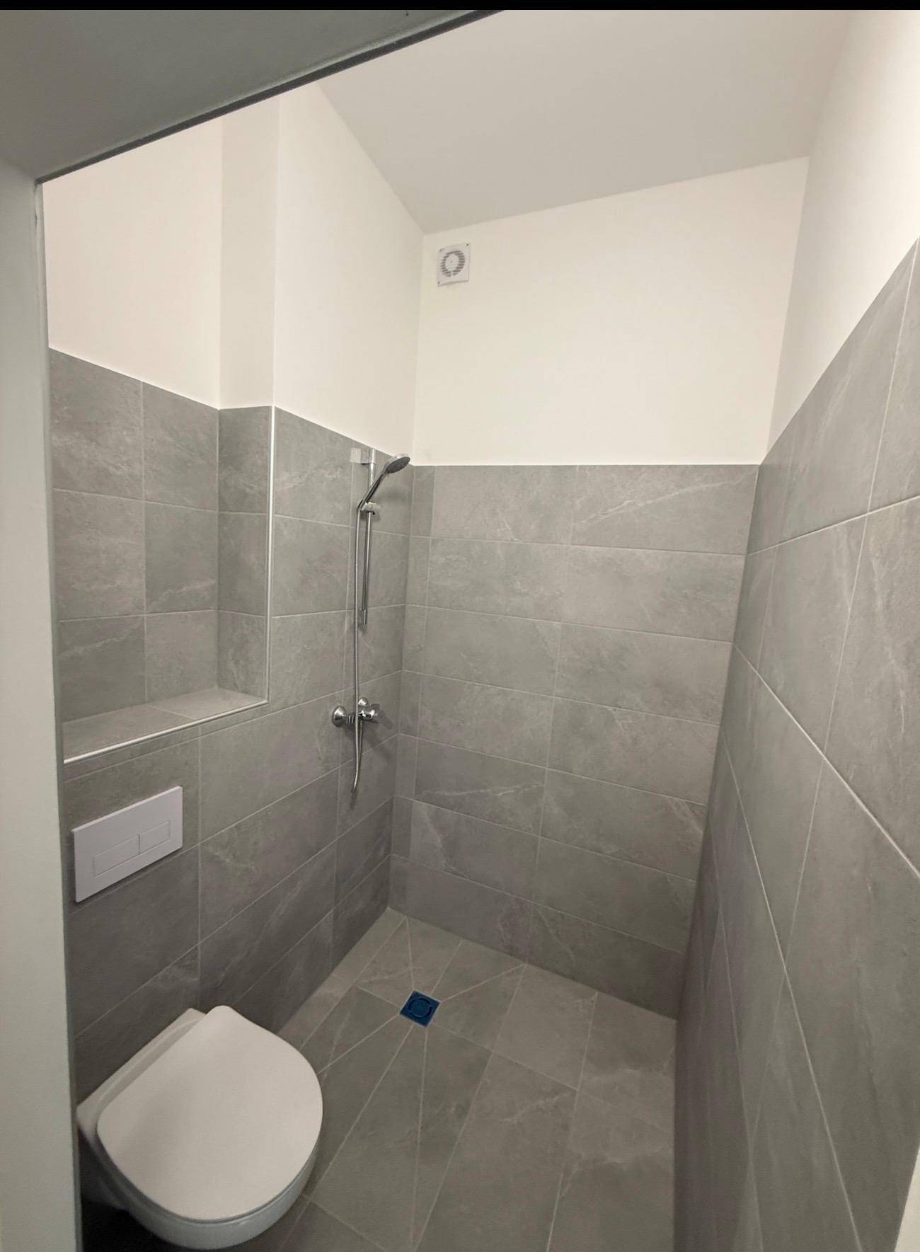 Modernes Badezimmer mit Duschbereich, Hänge-WC und grauen Wand- und Bodenfliesen.