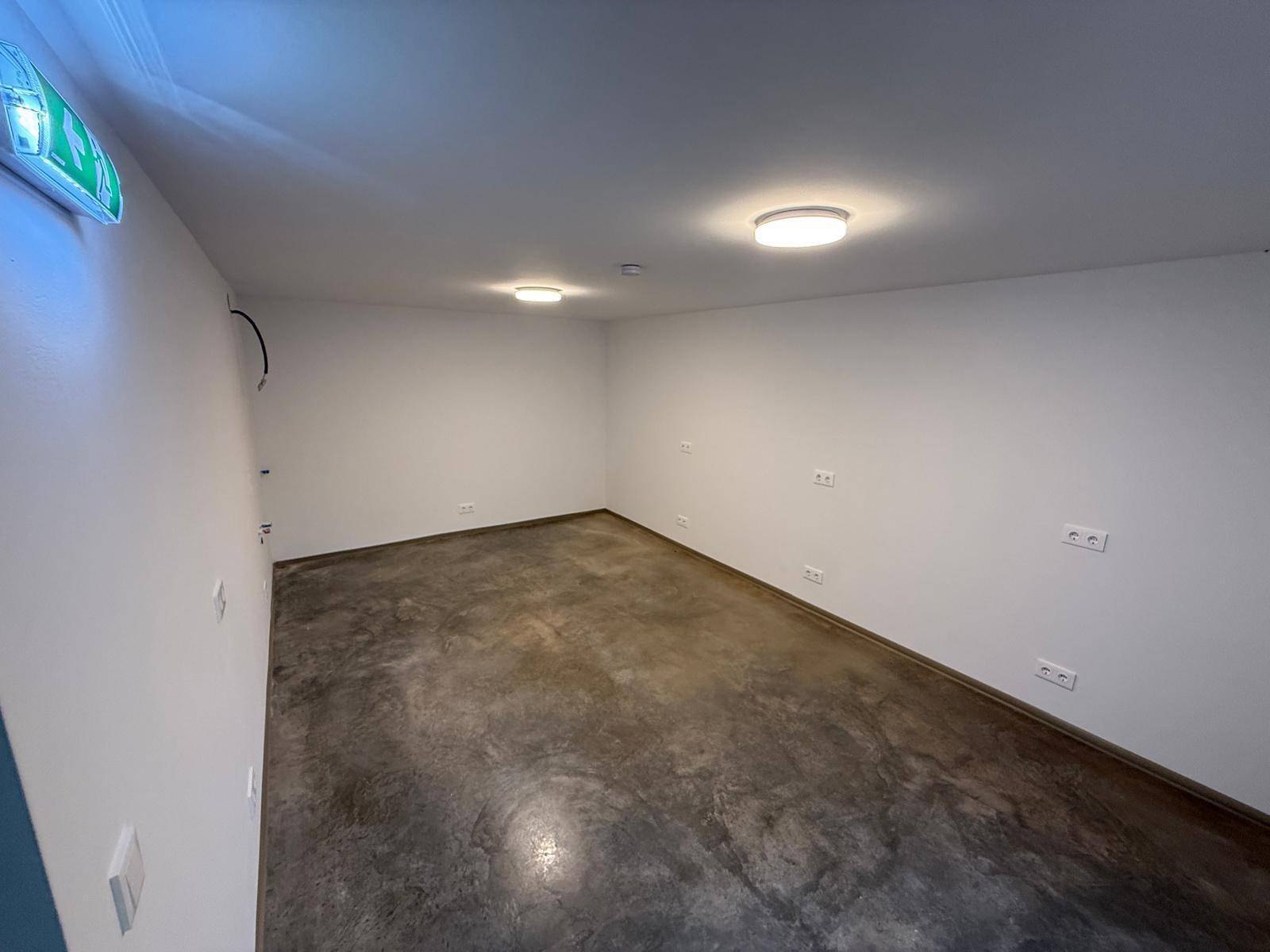 Kleiner, heller Abstellraum mit Betonboden und Deckenleuchten, ideal für Lagerzwecke.