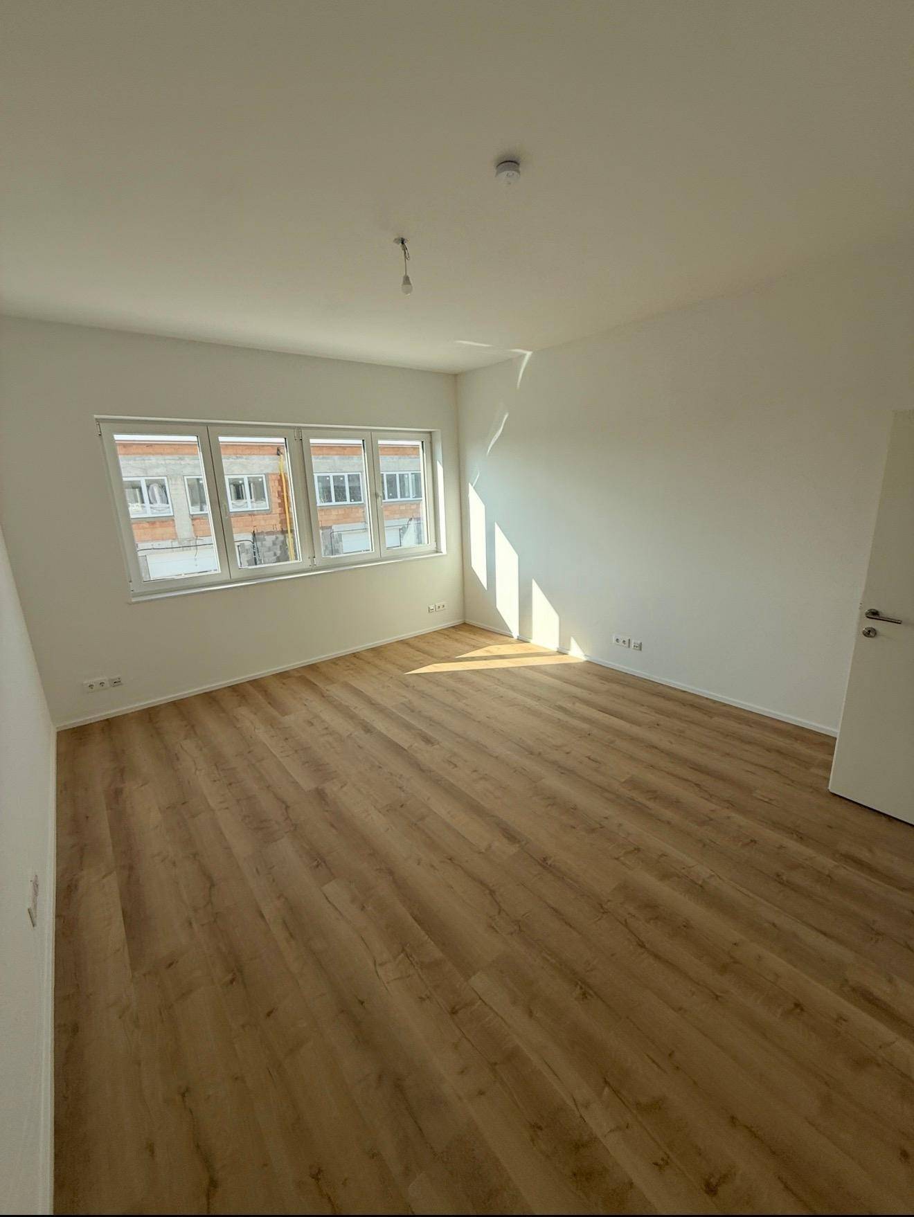 Heller Büroraum mit Laminatboden und großen Fenstern, die viel Sonnenlicht hereinlassen.