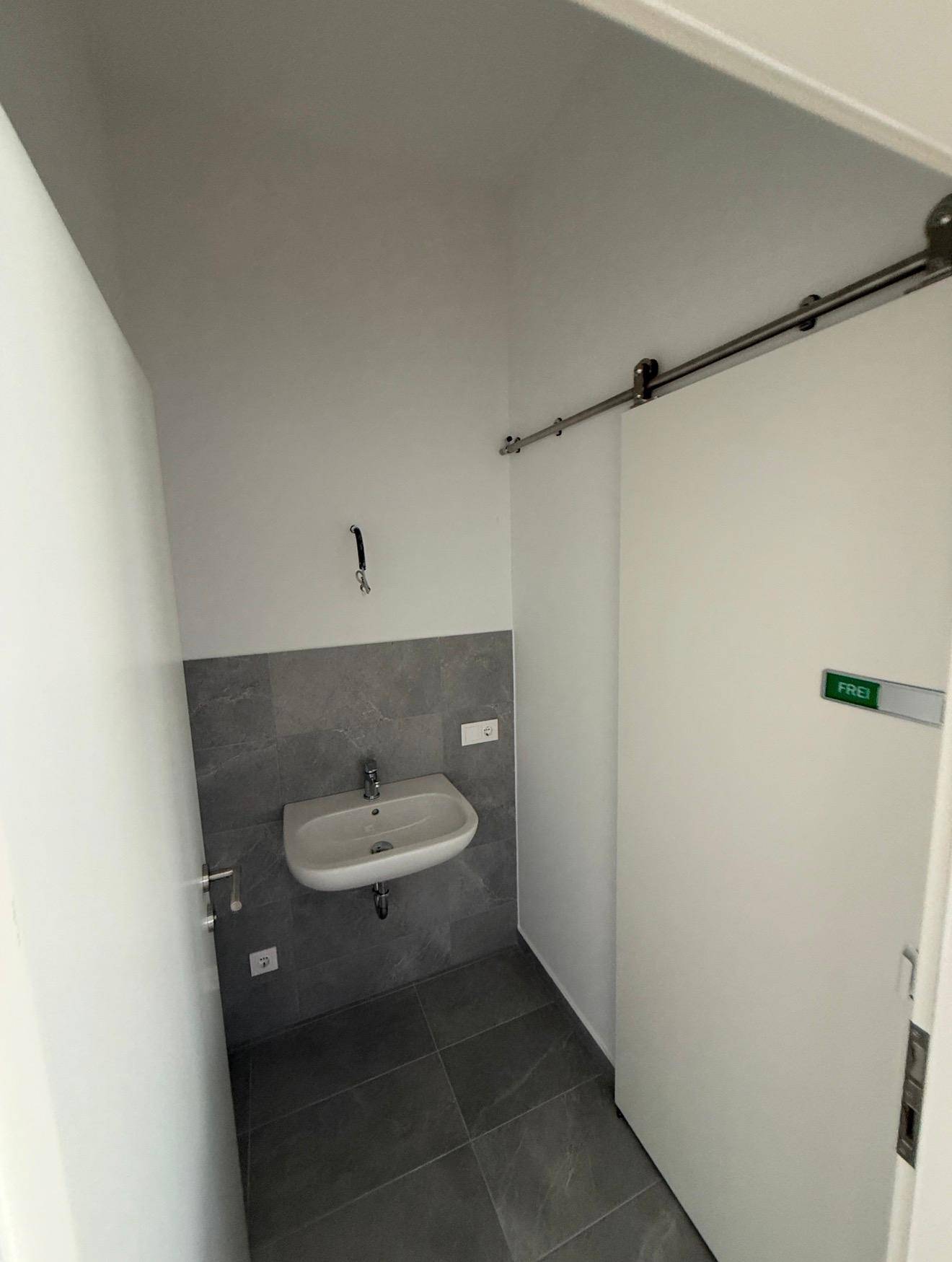 Kleine, moderne Toilette mit Waschbecken und grauen Fliesen an Wand und Boden.