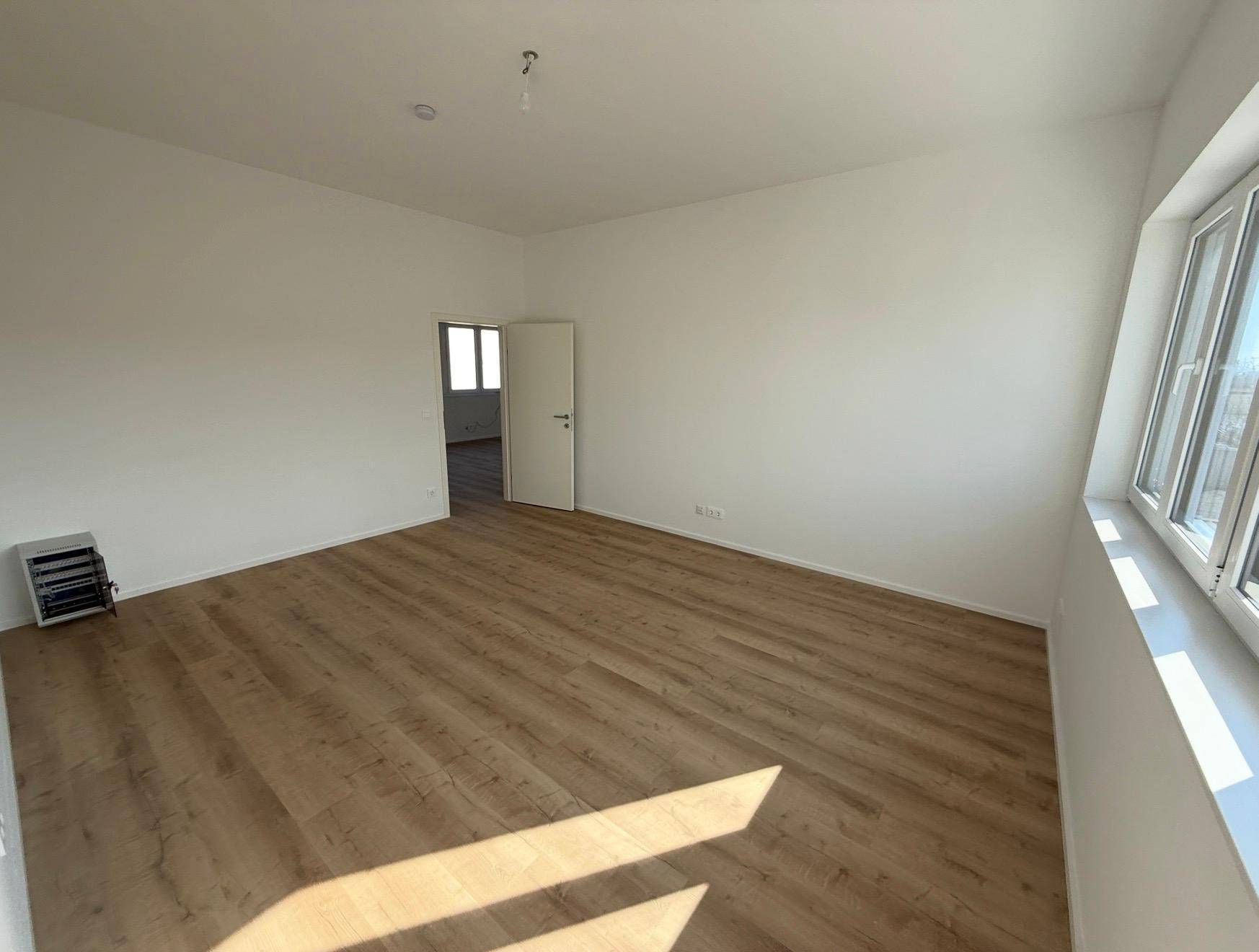 Heller, leerer Büroraum mit Laminatboden und großen Fenstern, bereit zur Einrichtung.