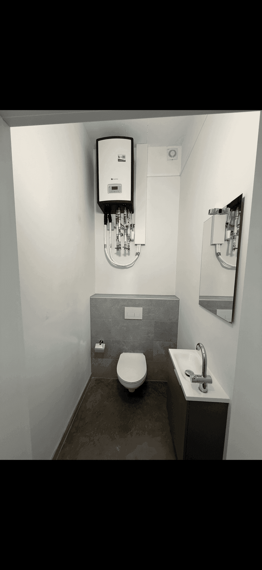 Kleine, moderne Toilette mit Hänge-WC, Waschbecken und Warmwasserbereiter an der Wand.