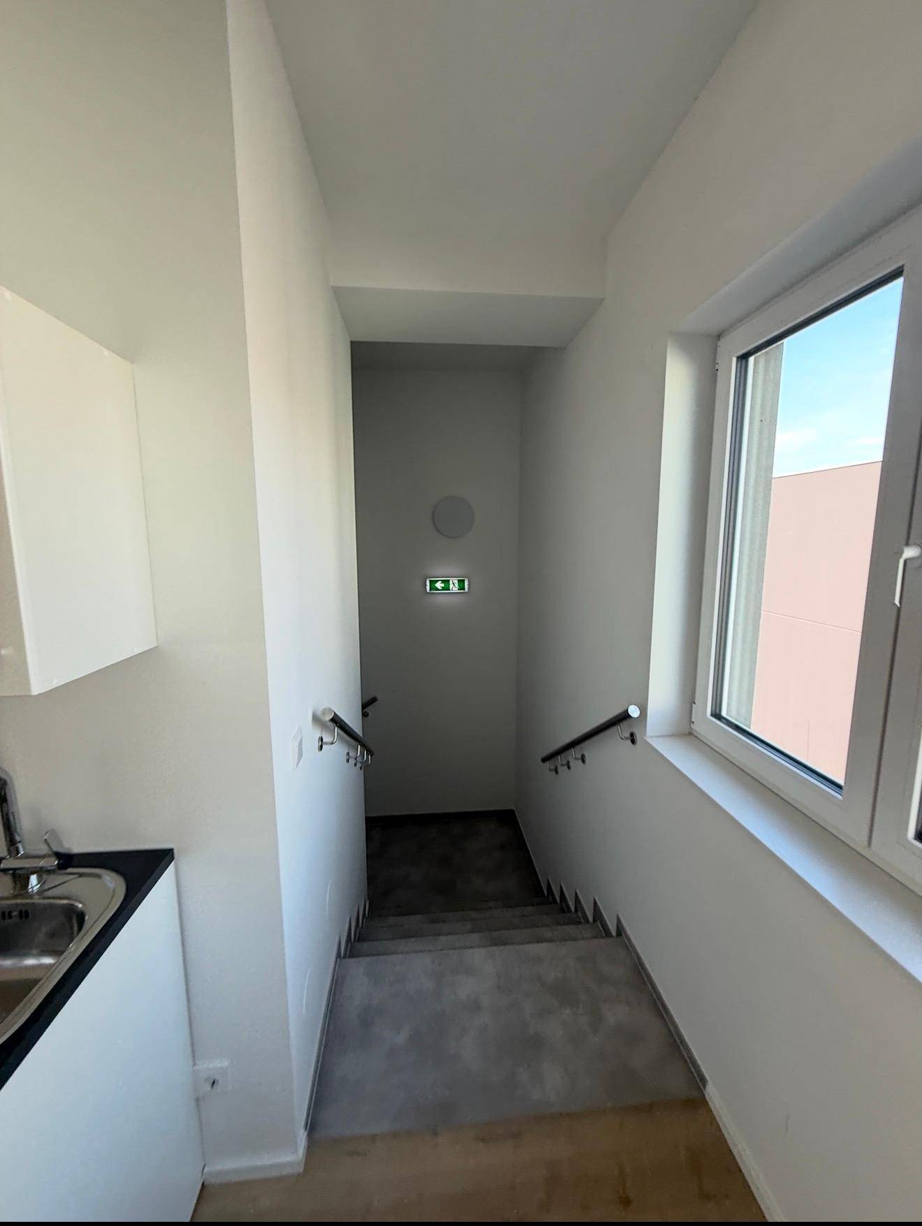 Treppenhaus mit Betonstufen und Handläufen, daneben eine kleine Küchenzeile.