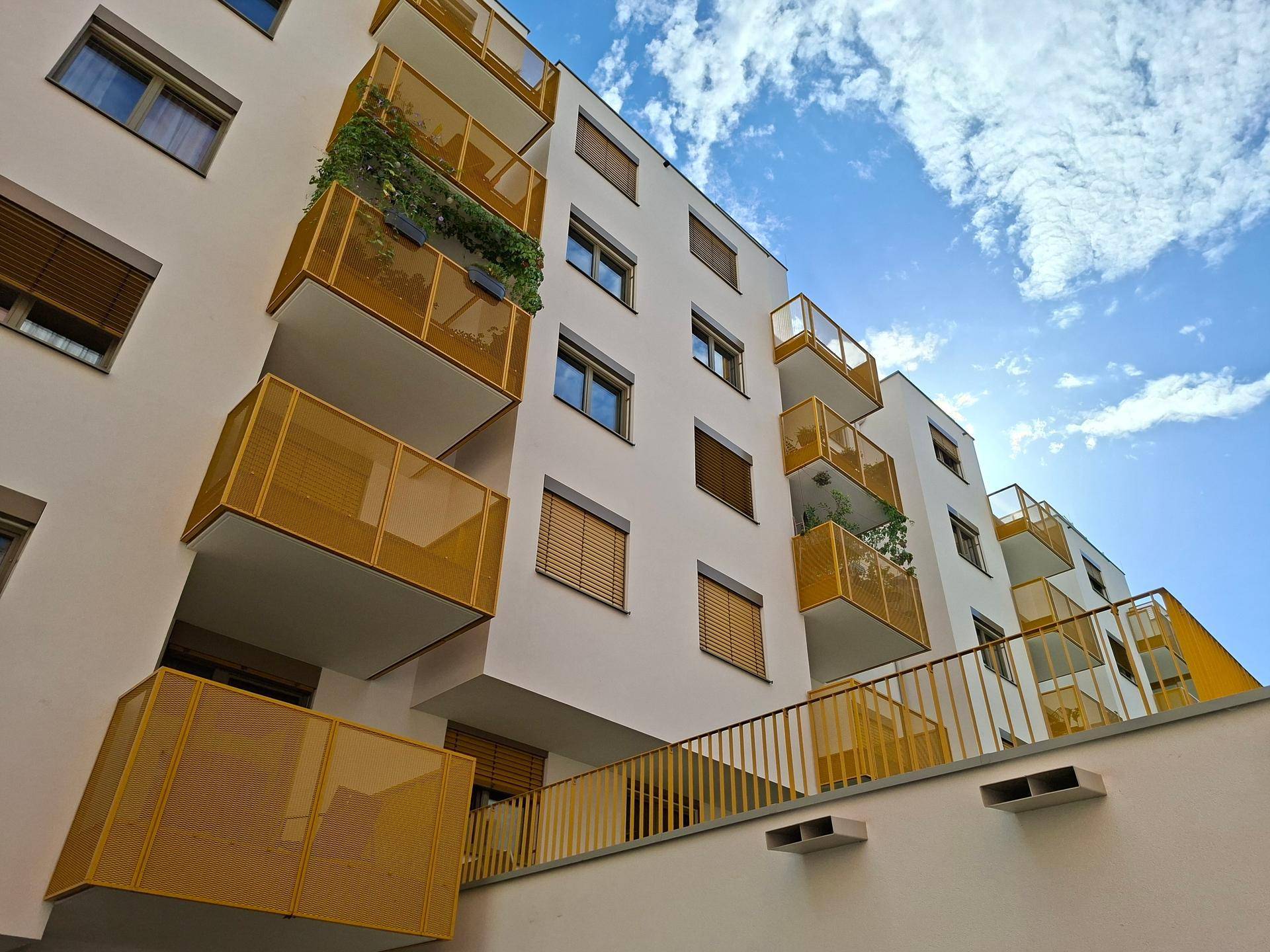 Moderne Architektur mit mehreren gelben Balkonen unter blauem Himmel und leichter Bewölkung.
