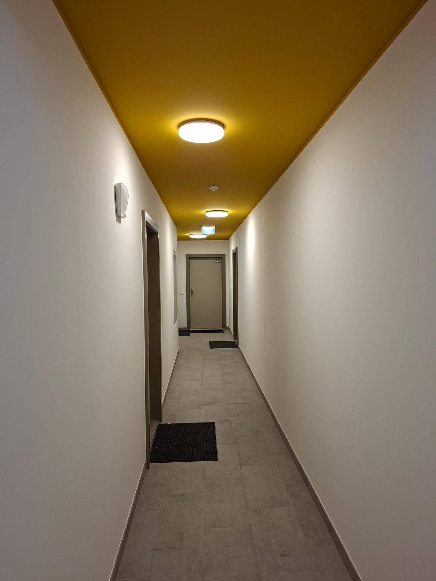 Langer Flur mit gelber Decke, hellen Wänden und Fliesenboden.