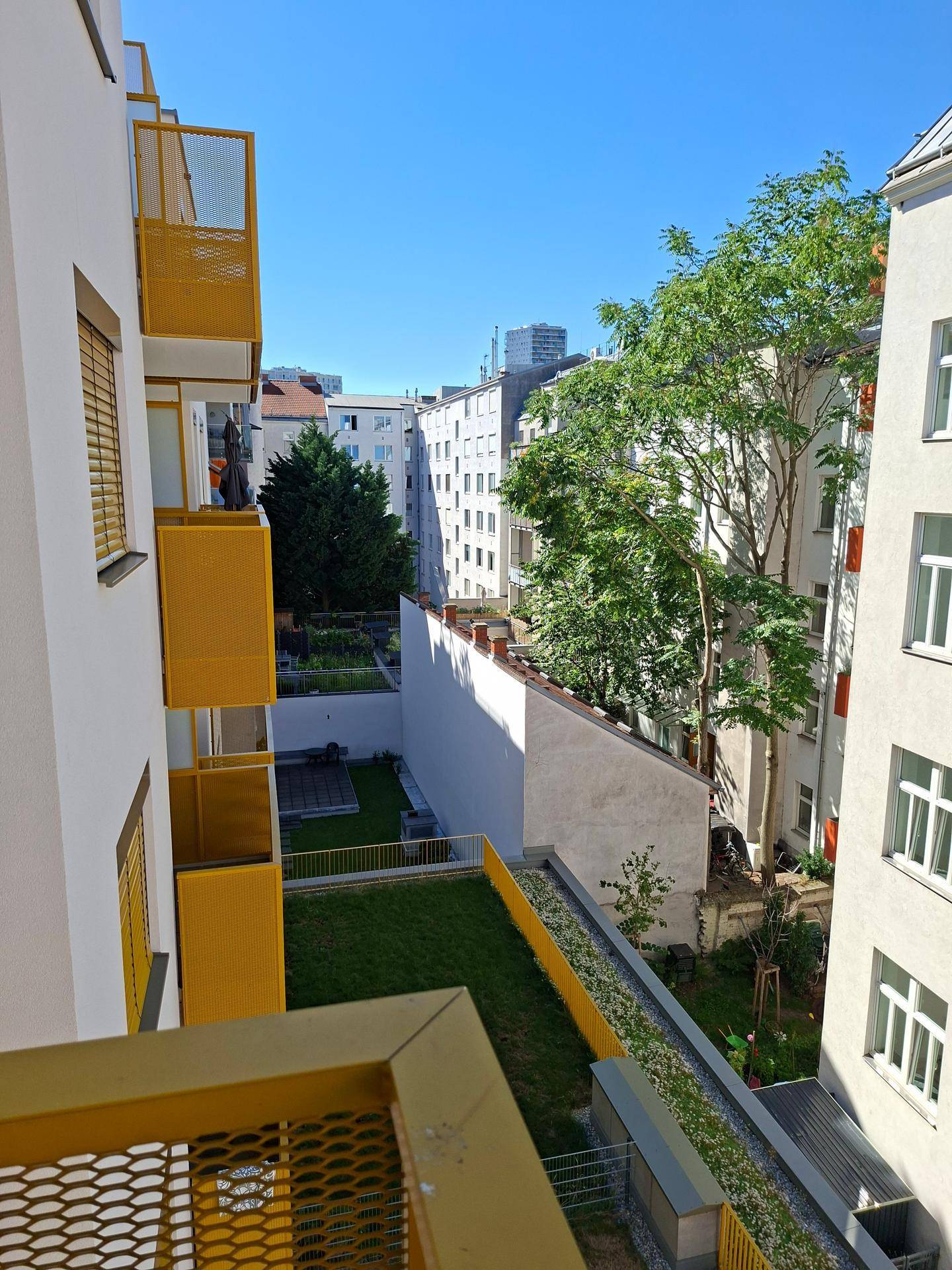 Blick von einem Balkon auf einen begrünten Innenhof mit weiteren Gebäuden im Hintergrund.