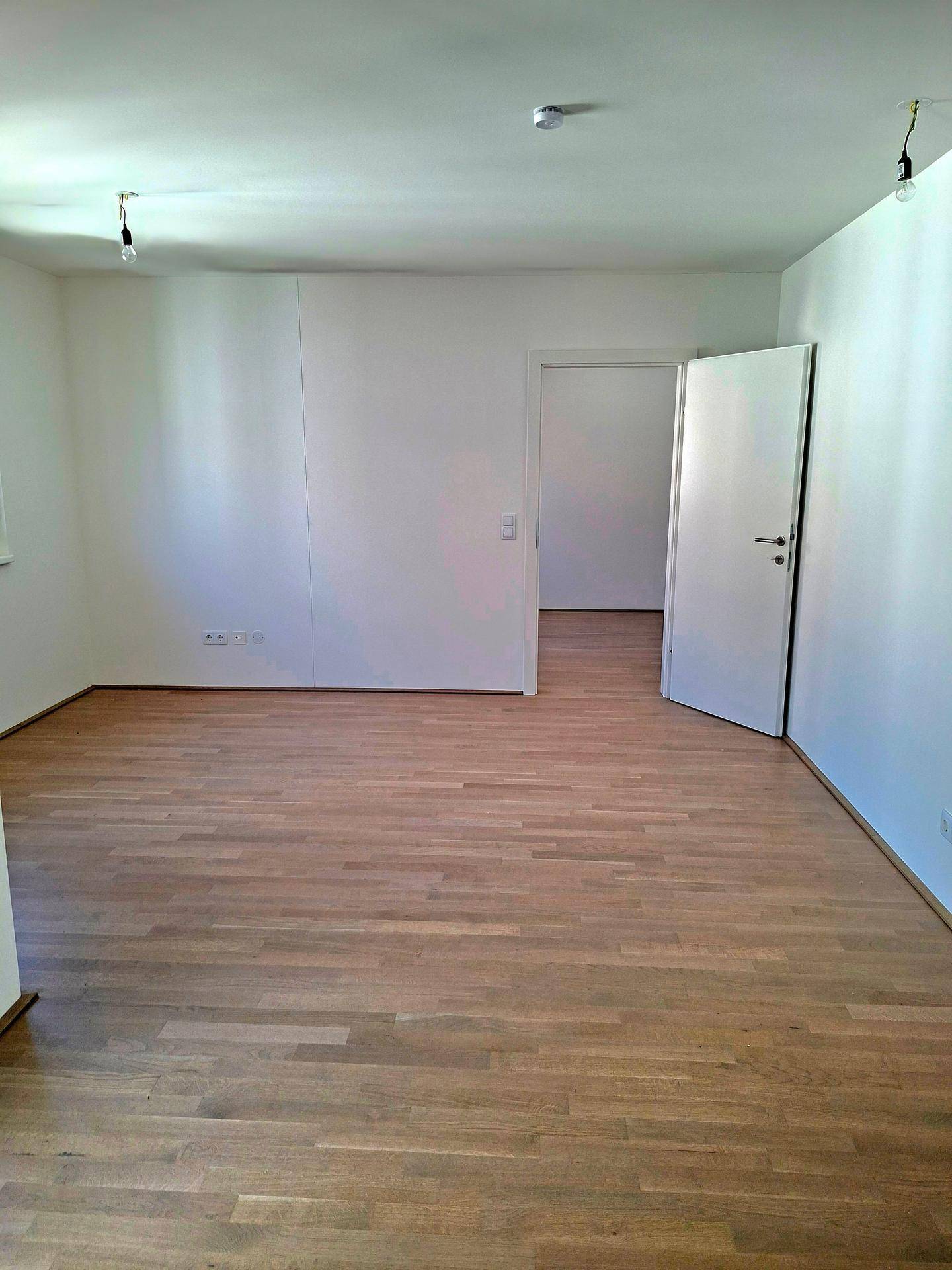Leerer Raum mit hellem Parkettboden und weißer Tür, bereit zur individuellen Gestaltung.