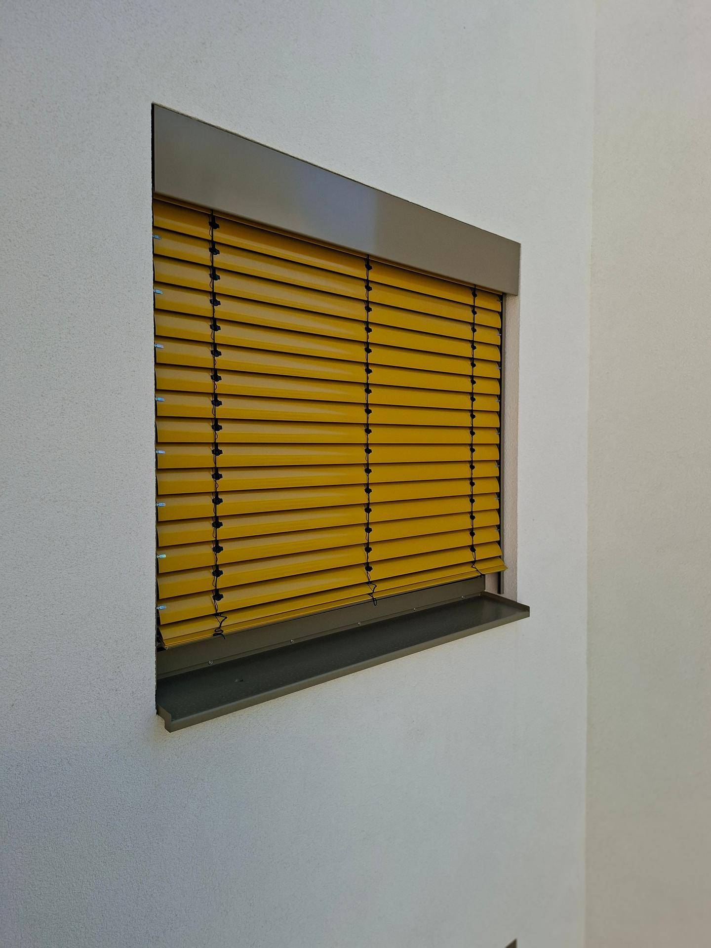 Fenster mit gelben Außenjalousien an einer weißen Fassade.