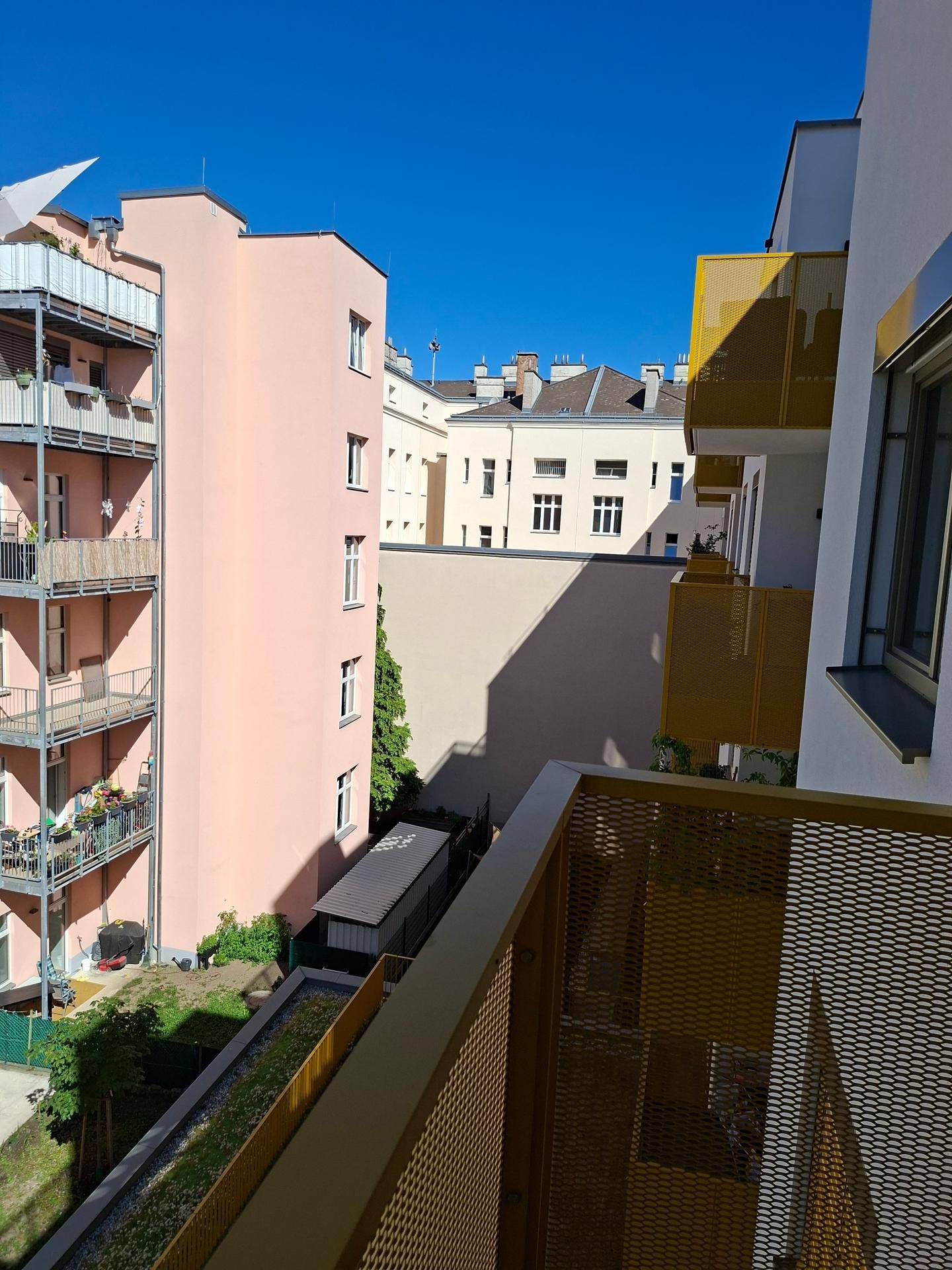 Aussicht von einem Balkon auf benachbarte Gebäude und einen kleinen Gartenbereich.