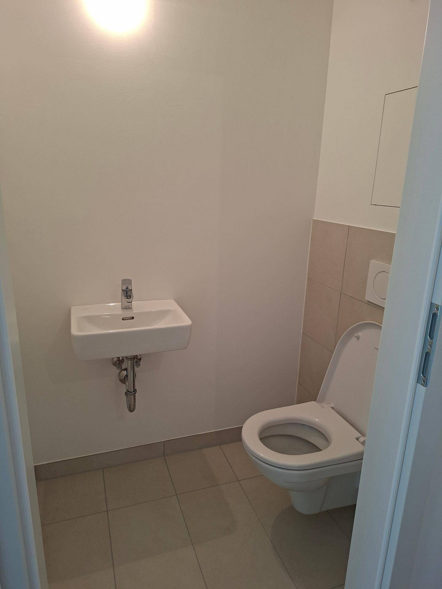 Kleines Gäste-WC mit Toilette, Wandwaschbecken und hellen Fliesen.