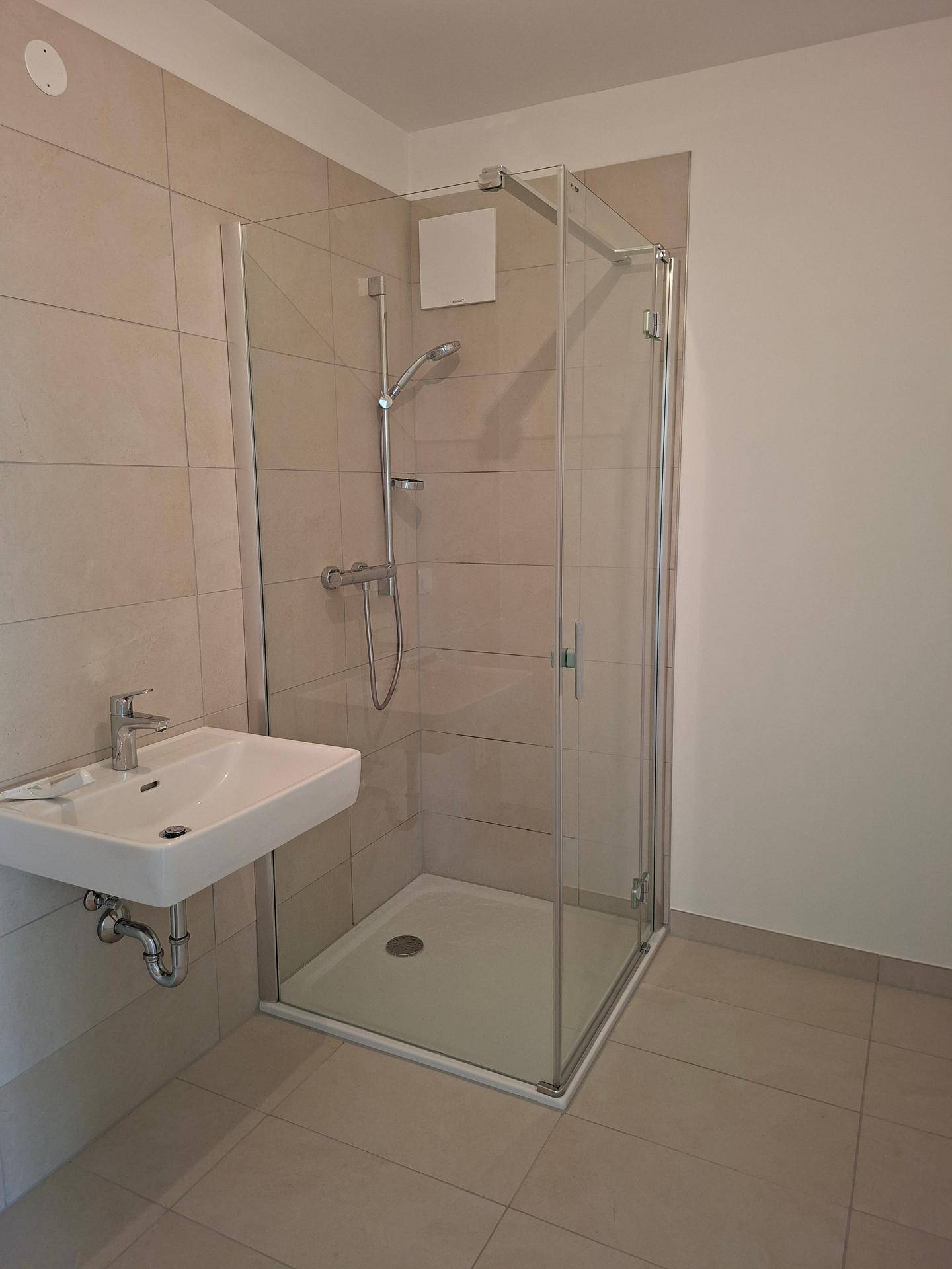 Modernes Badezimmer mit Duschkabine, Wandwaschbecken und hellen Fliesen.