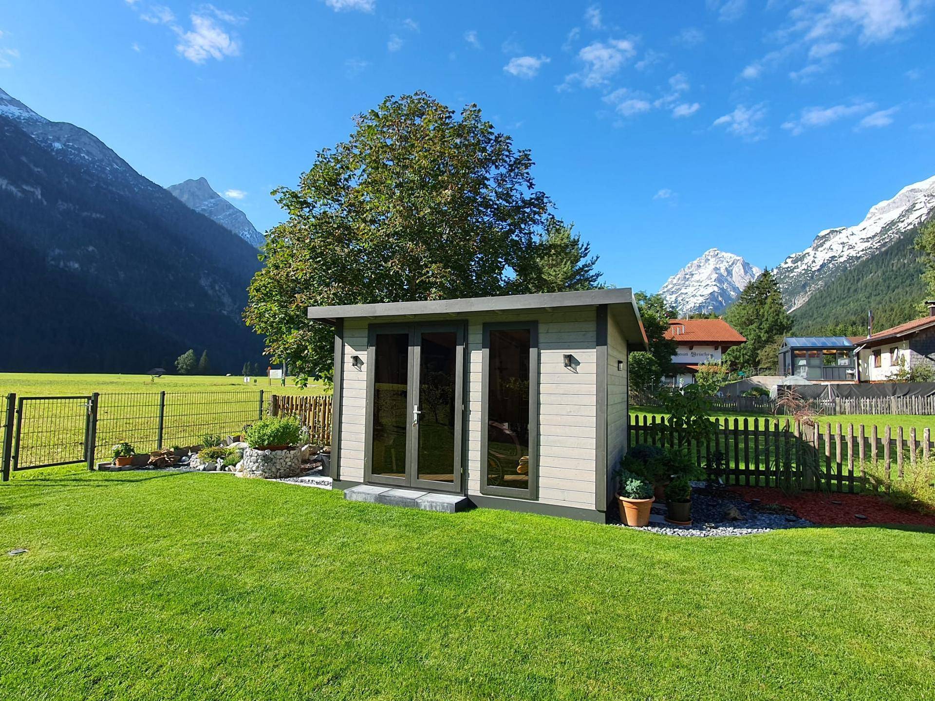 Kleines Gartenhaus auf grünem Rasen mit Bergblick, ideal für Gartengeräte.