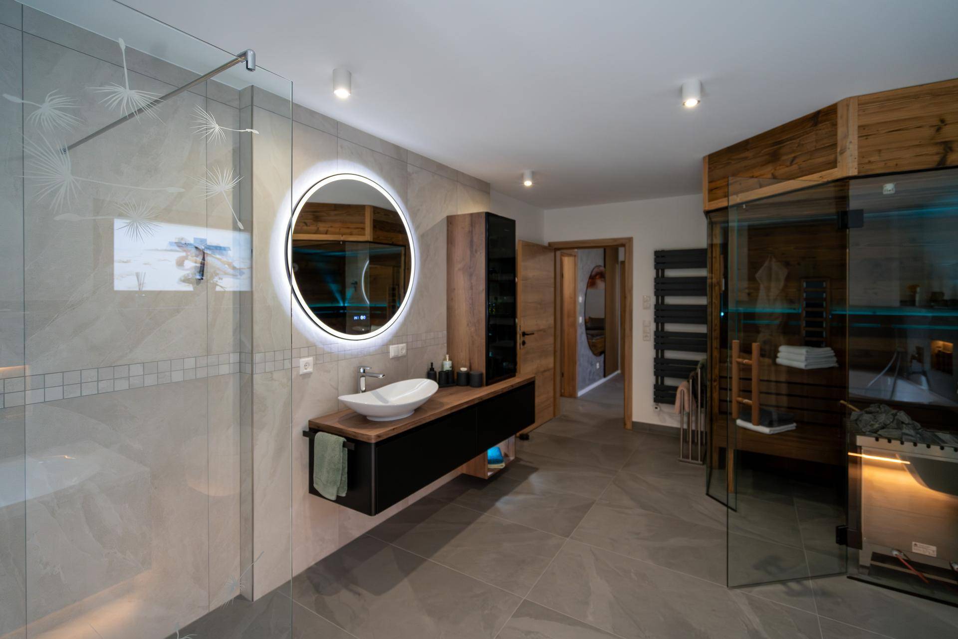 Modernes Badezimmer mit schwebendem Waschtisch, runden Spiegel und begehbarer Dusche.