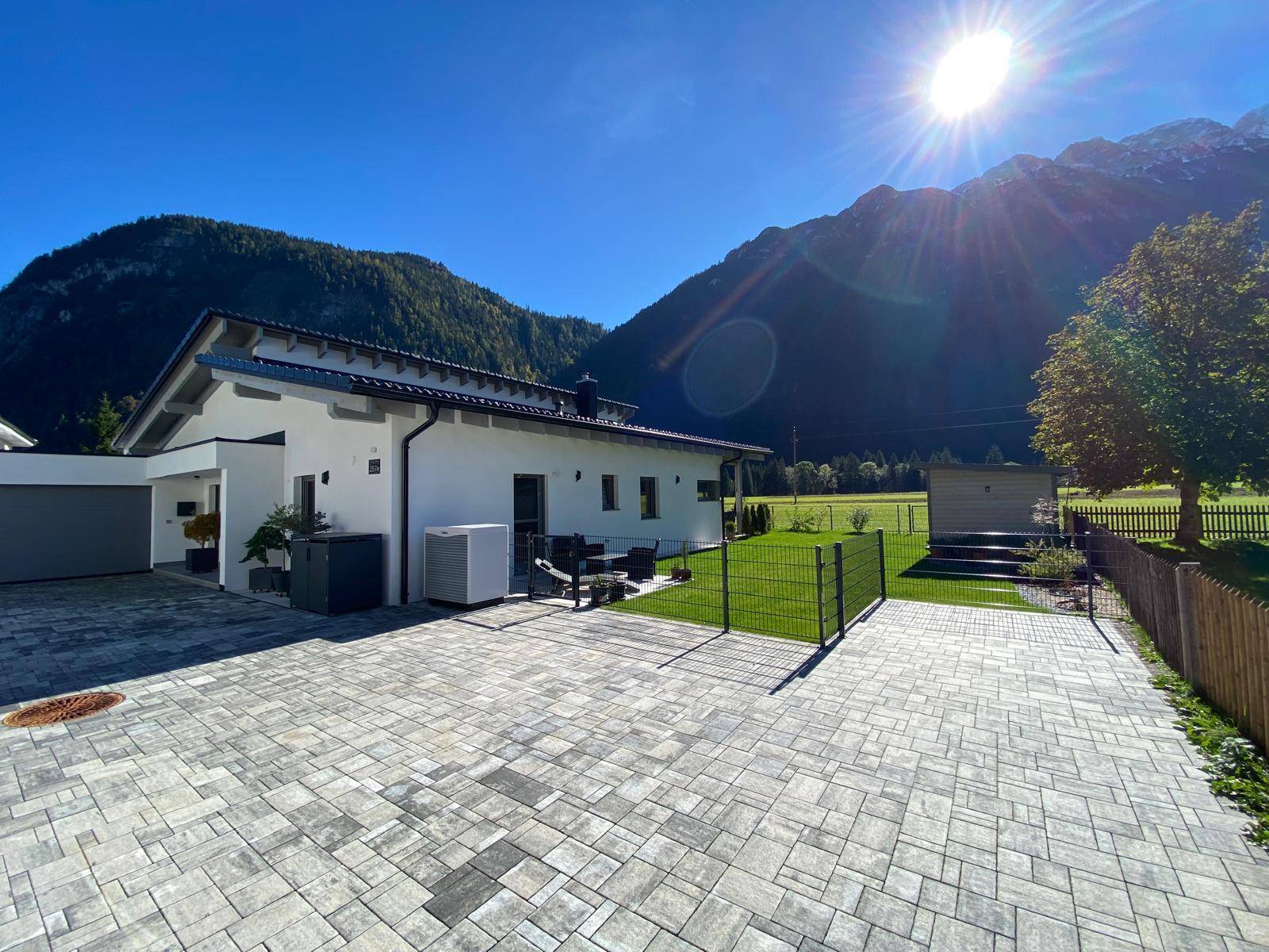 Rückansicht des Hauses mit gepflasterter Auffahrt, Garten und beeindruckendem Bergblick.