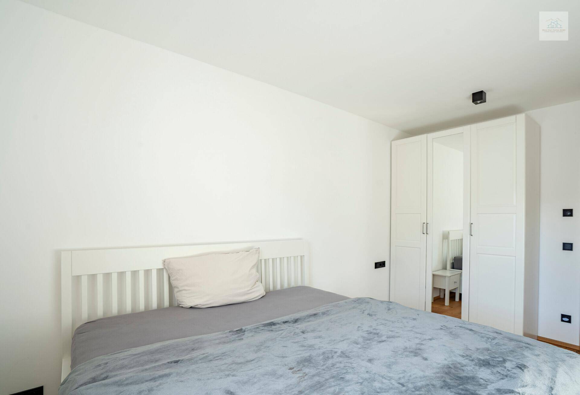 Gemütliches Schlafzimmer mit weißem Bett und Kleiderschrank, ideal für erholsame Nächte.