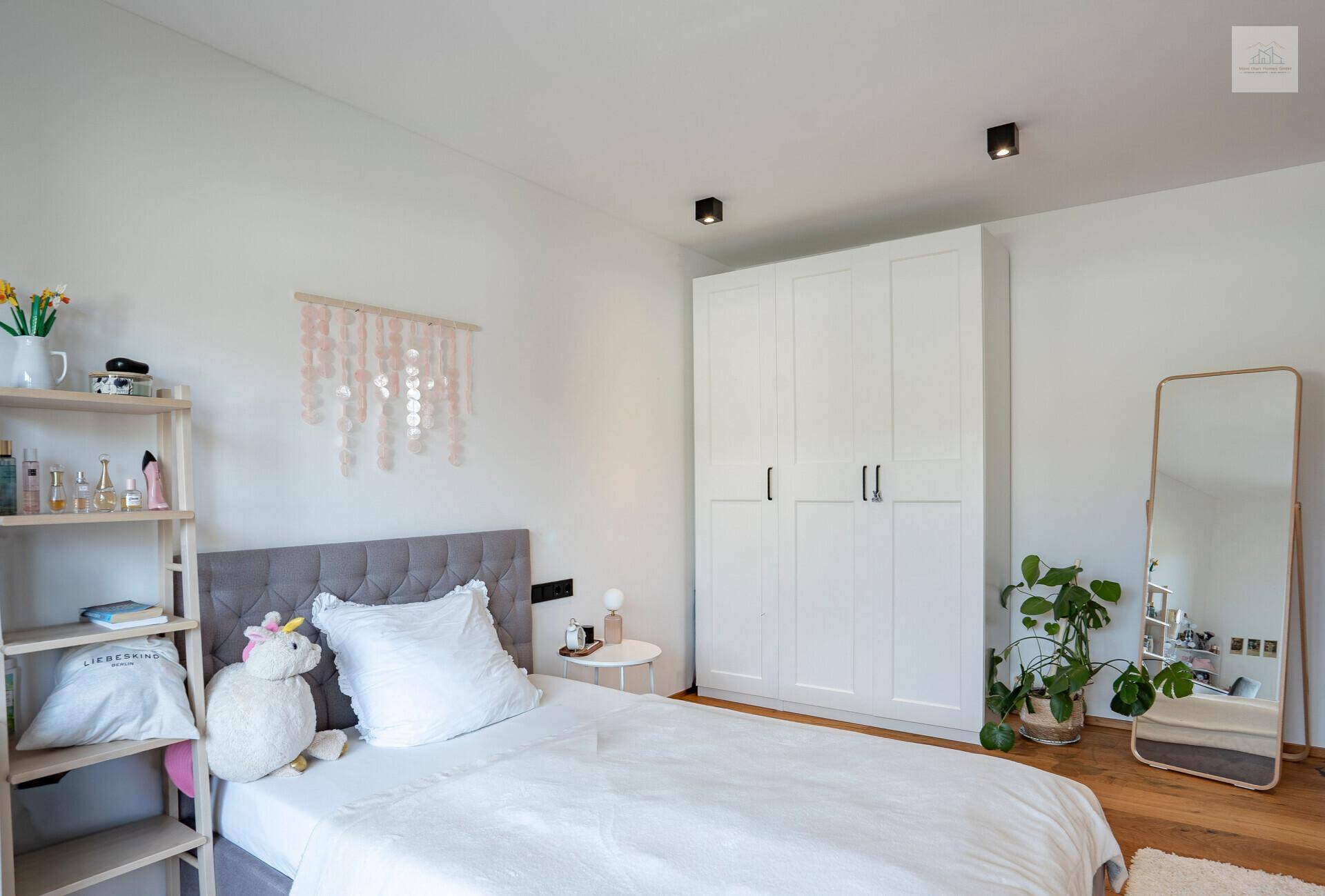 Freundliches Kinderzimmer mit Bett, weißem Kleiderschrank und dekorativen Elementen.