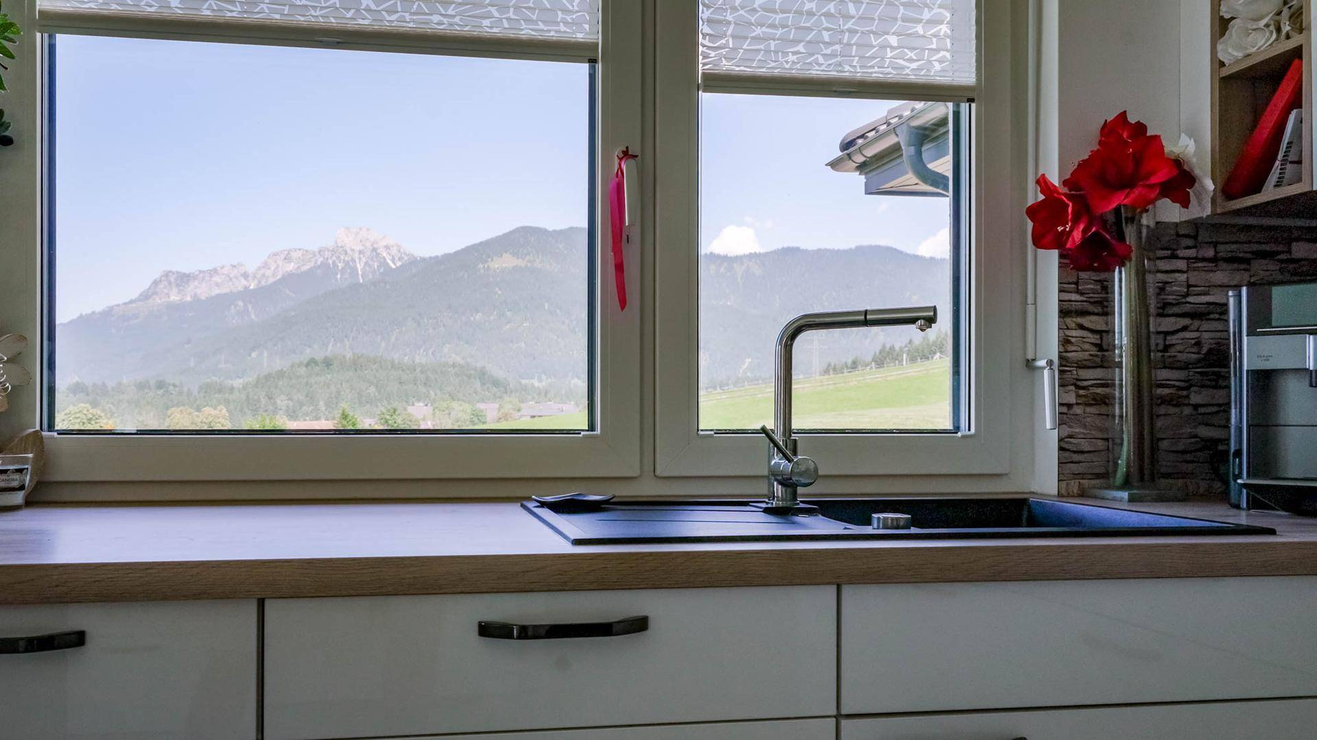 Helle Küche mit Spülbecken unter einem großen Fenster, das einen weiten Blick auf die Berge freigibt.