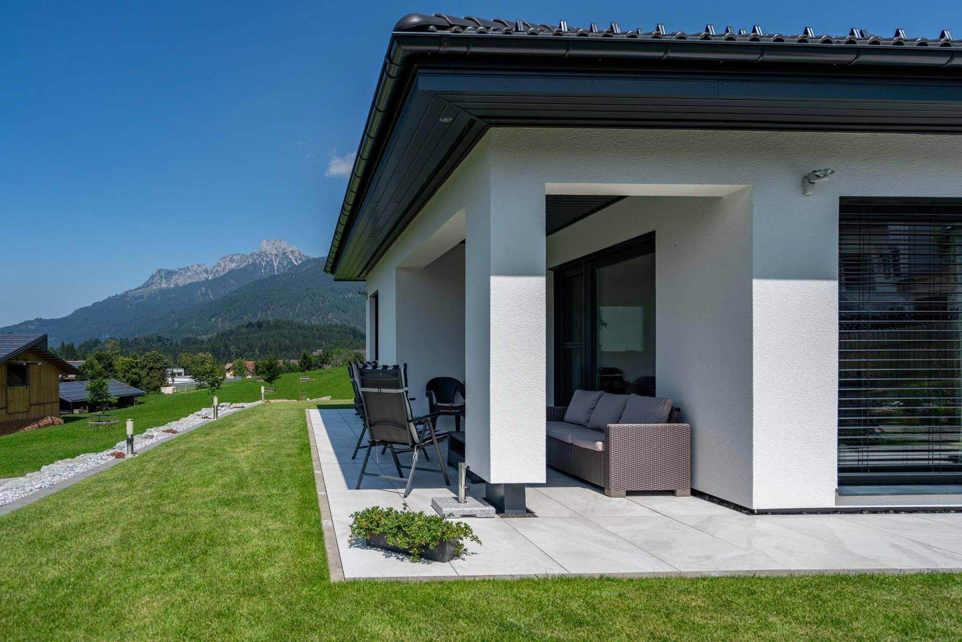 Überdachte Terrasse mit bequemen Sitzgelegenheiten und direktem Zugang zum Garten mit Bergblick.