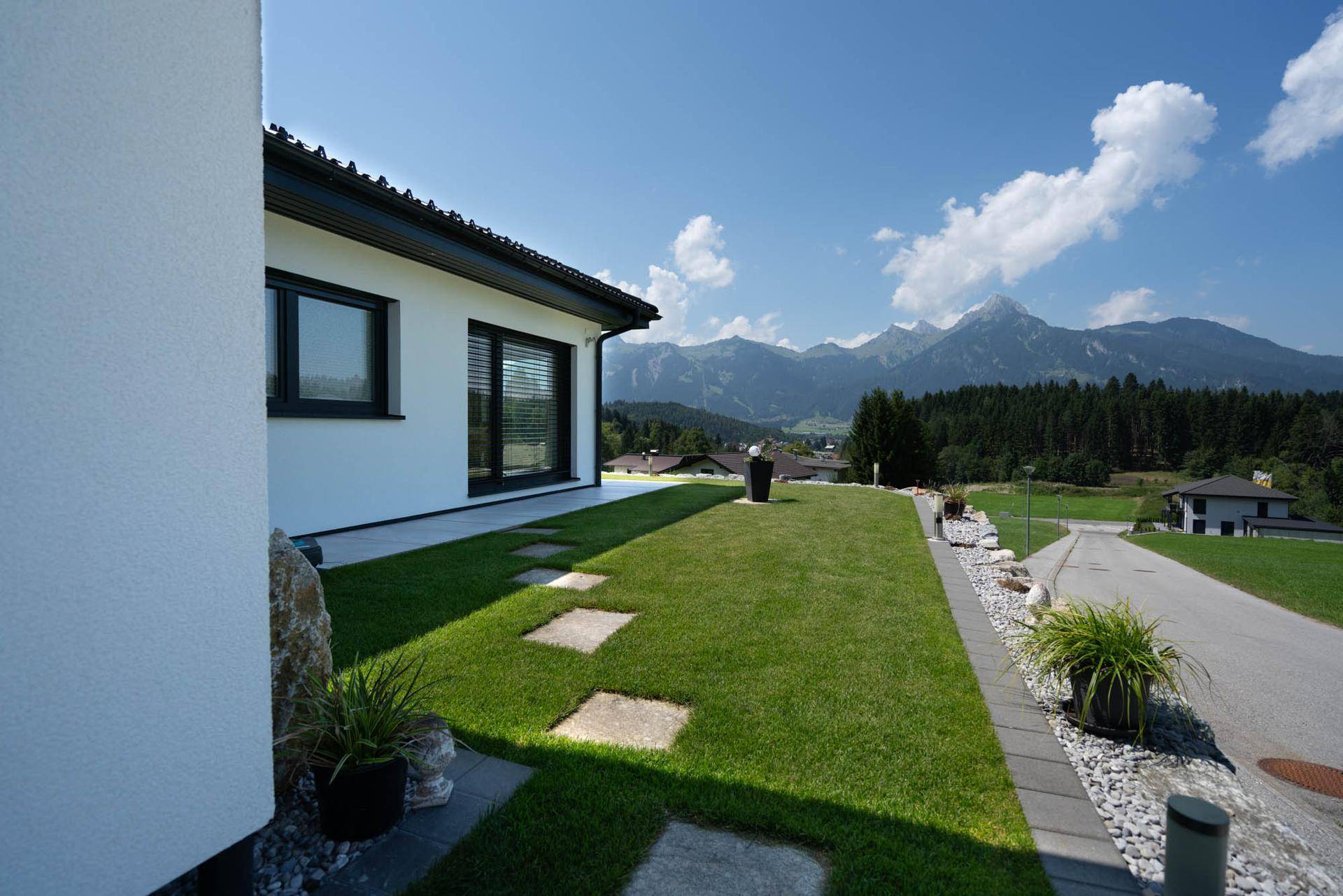 Gepflegter Rasenbereich mit Trittsteinen entlang des Hauses und weitem Blick auf die Berge.