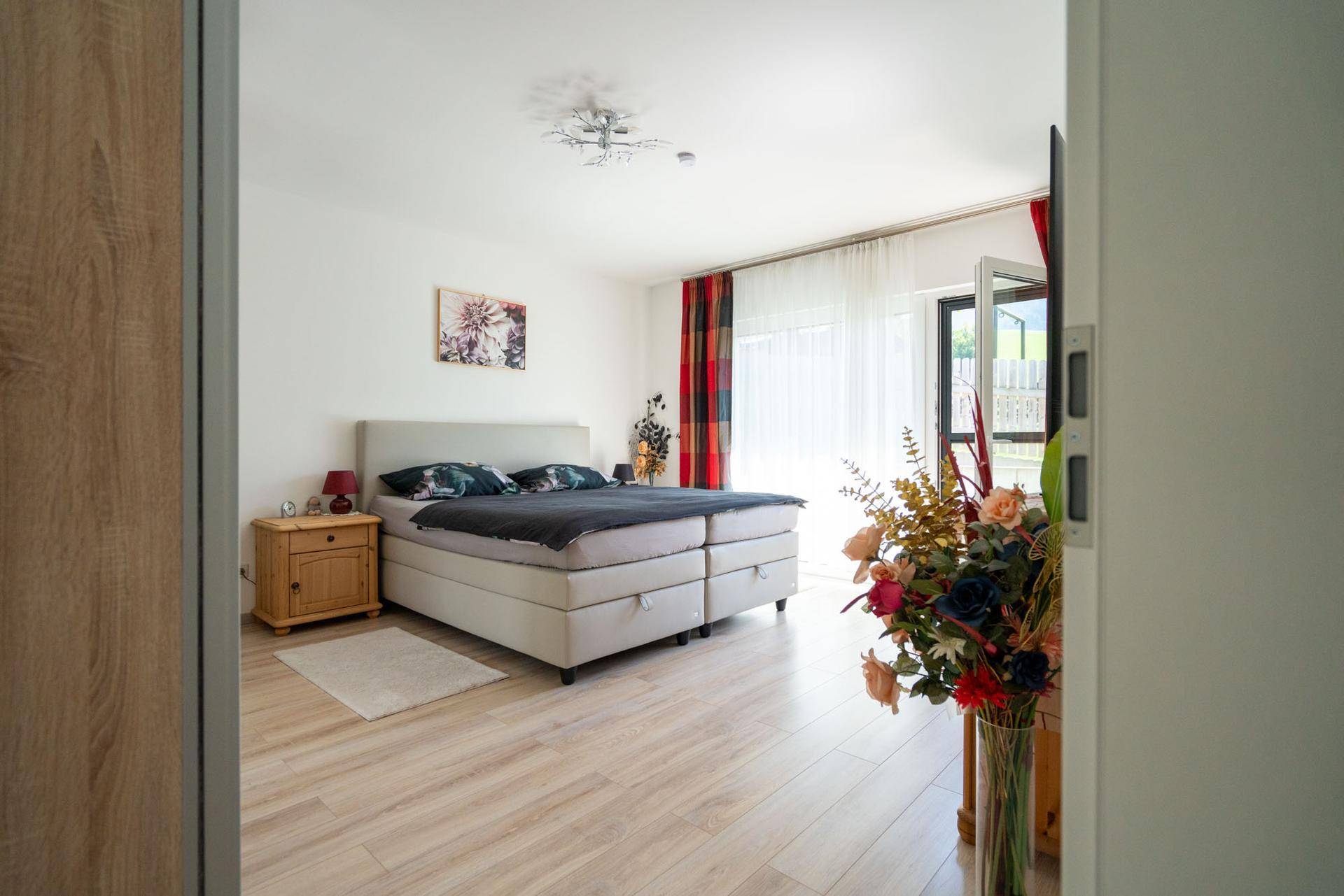Geräumiges Schlafzimmer mit großem Boxspringbett, hellem Boden und Zugang zu einem Außenbereich.