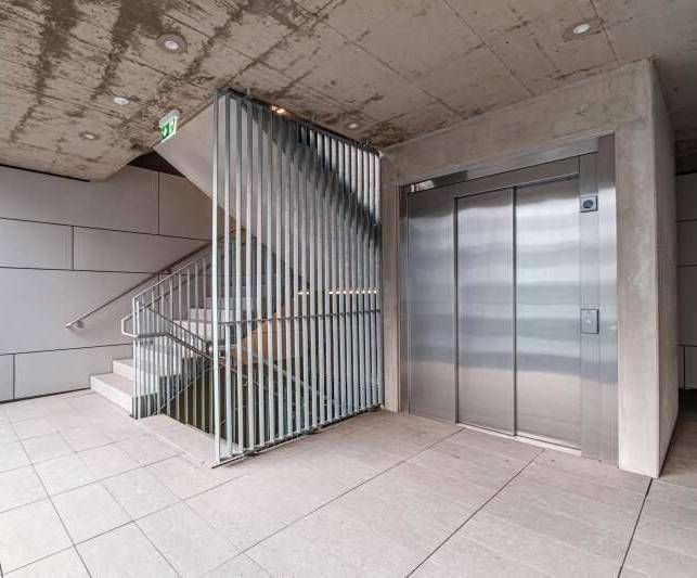 Moderner Eingangsbereich mit Aufzug und Treppenhaus in einem Wohngebäude.
