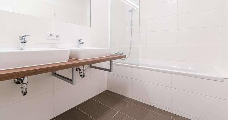 Helles Badezimmer mit Doppelwaschbecken, Badewanne und weißen Fliesen.