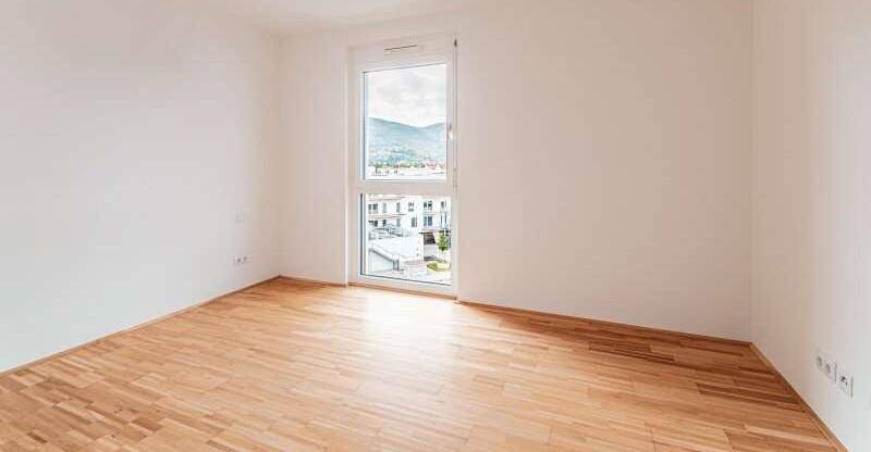 Leerer Raum mit Holzboden und großem Fenster mit Blick auf die Berge.