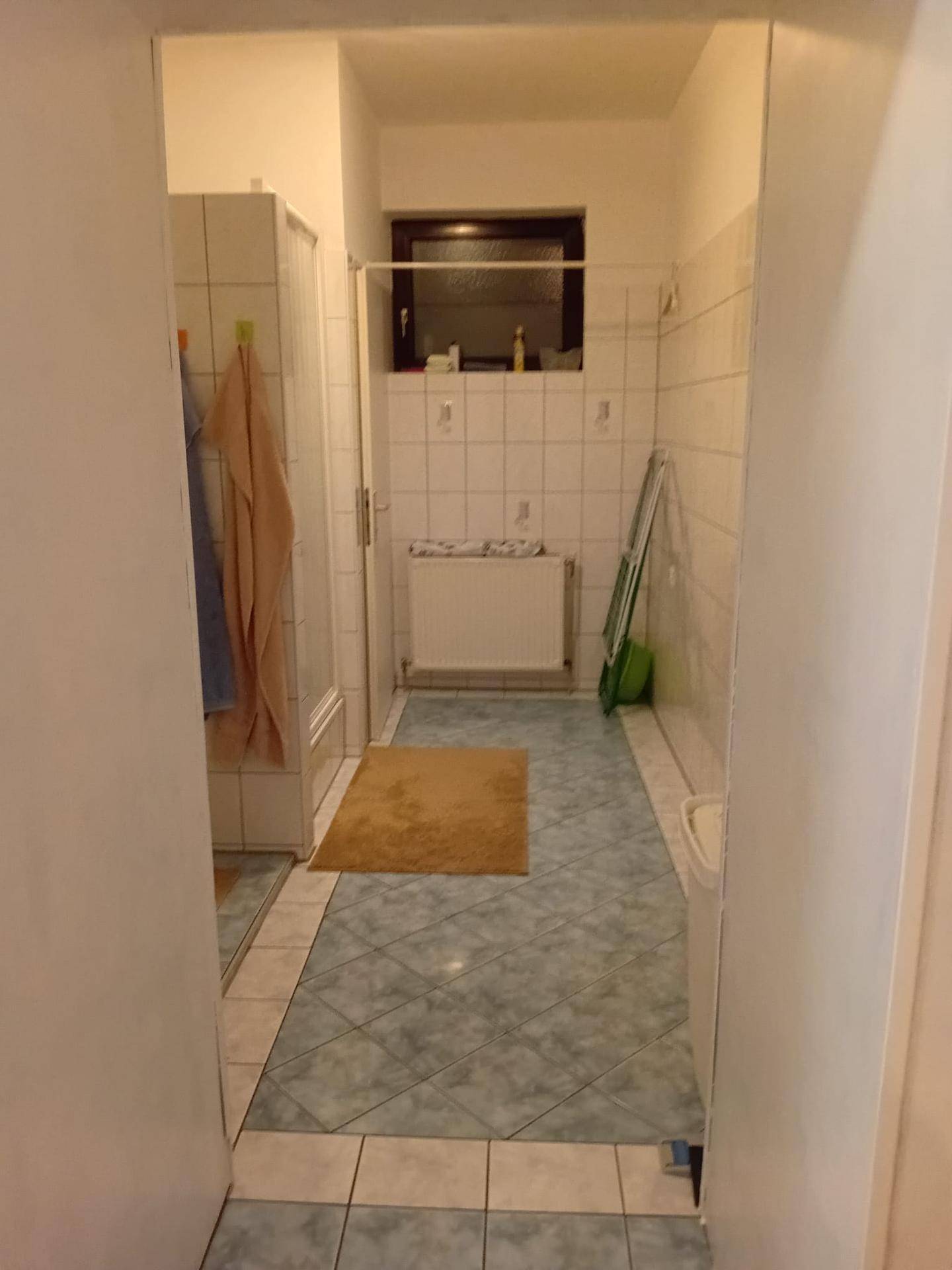 Badezimmer mit Duschkabine, Fenster und hellblauen Fliesen auf dem Boden.