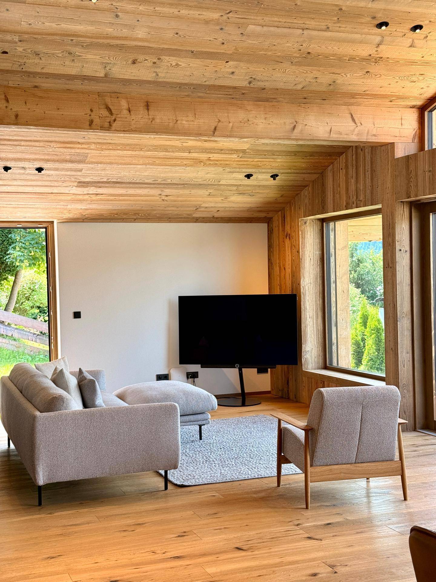 Gemütliches Wohnzimmer mit modernem Sofa, Fernseher und Holzbalkendecke.