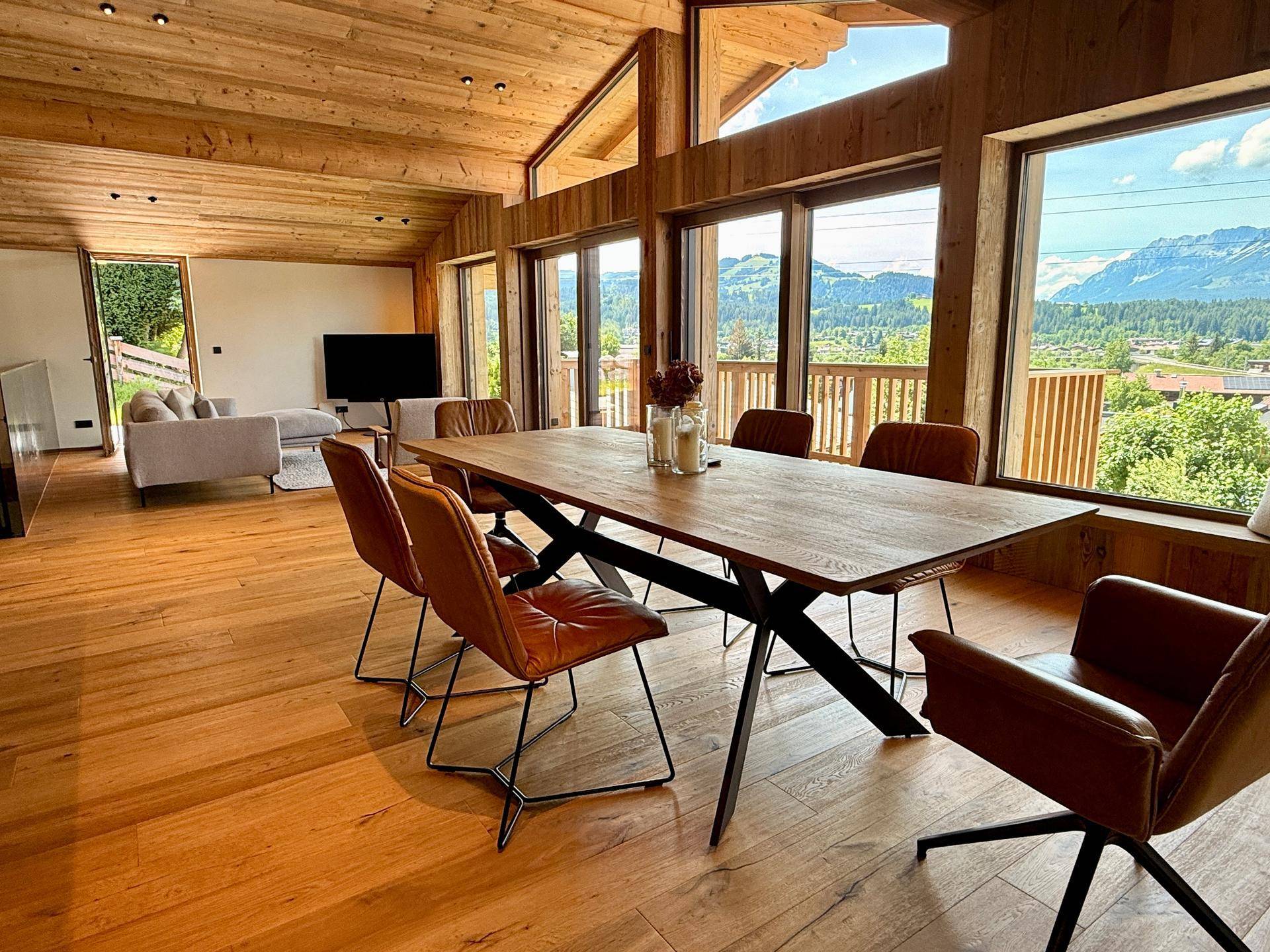 Heller Wohn-Essbereich mit großem Esstisch, Holzboden und Panoramablick auf die Berge.