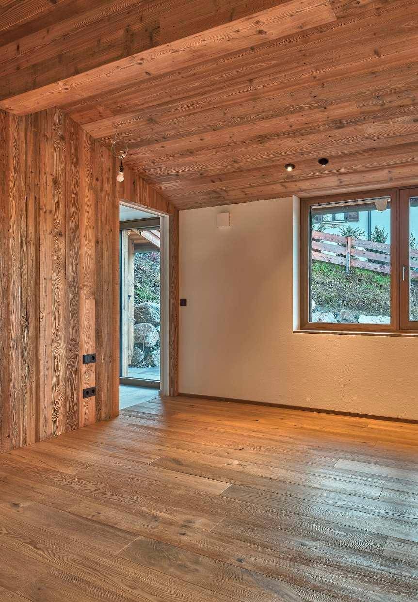 Helles Zimmer mit Holzboden, Holzwand und Fenster mit Blick ins Grüne.