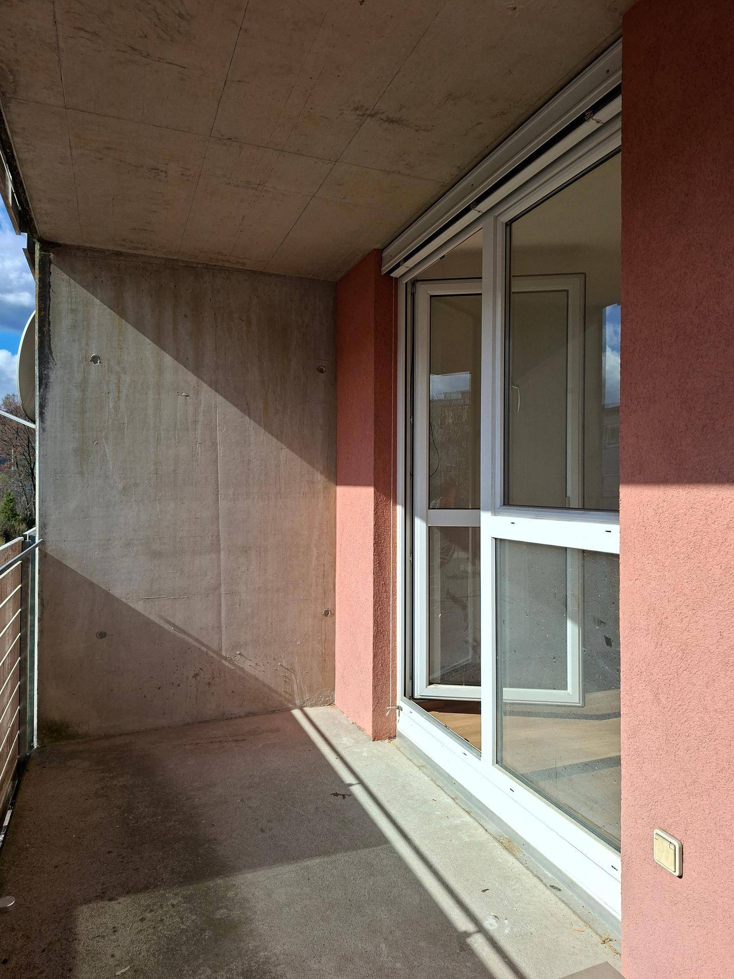 Sonniger Balkon mit Betonwänden und Zugang zum Innenbereich der Wohnung.