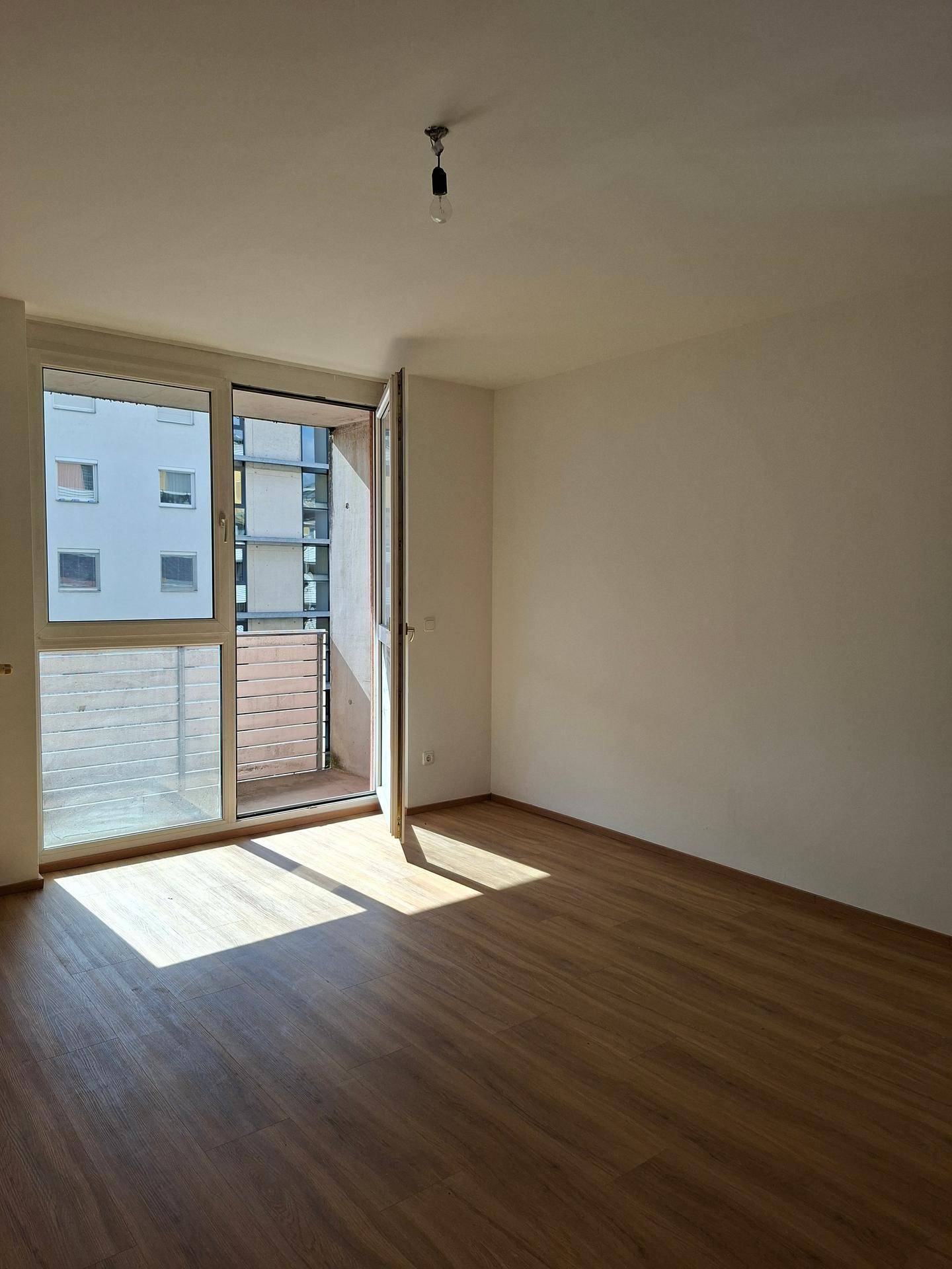 Heller, leerer Raum mit Laminatboden und Zugang zu einem kleinen Balkon.