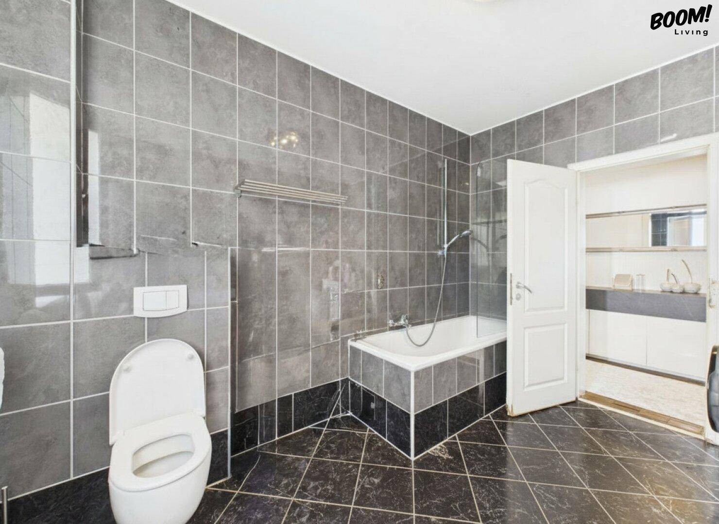 Modernes Badezimmer mit grauen Fliesen, Badewanne und separatem WC-Bereich.