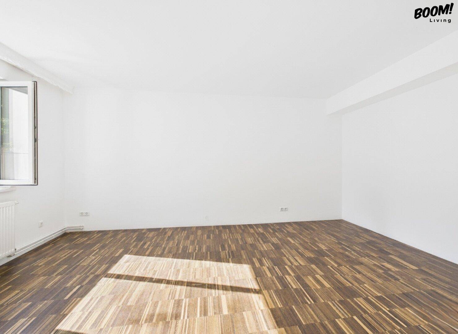 Heller, leerer Raum mit Holzboden und geöffnetem Fenster, bietet frische Luft und Licht.
