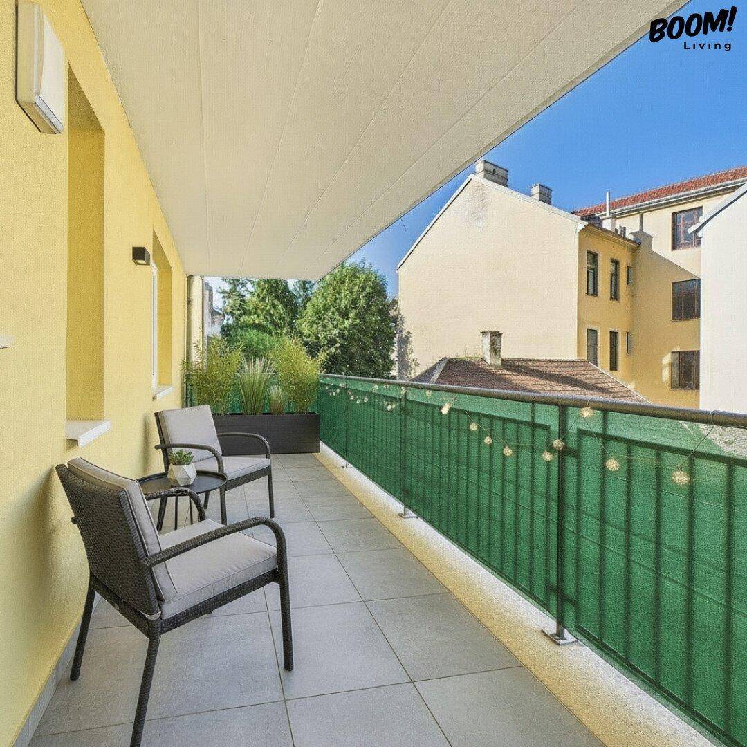 Sonniger Balkon mit Fliesenboden und Sitzgelegenheiten, umgeben von städtischer Architektur.