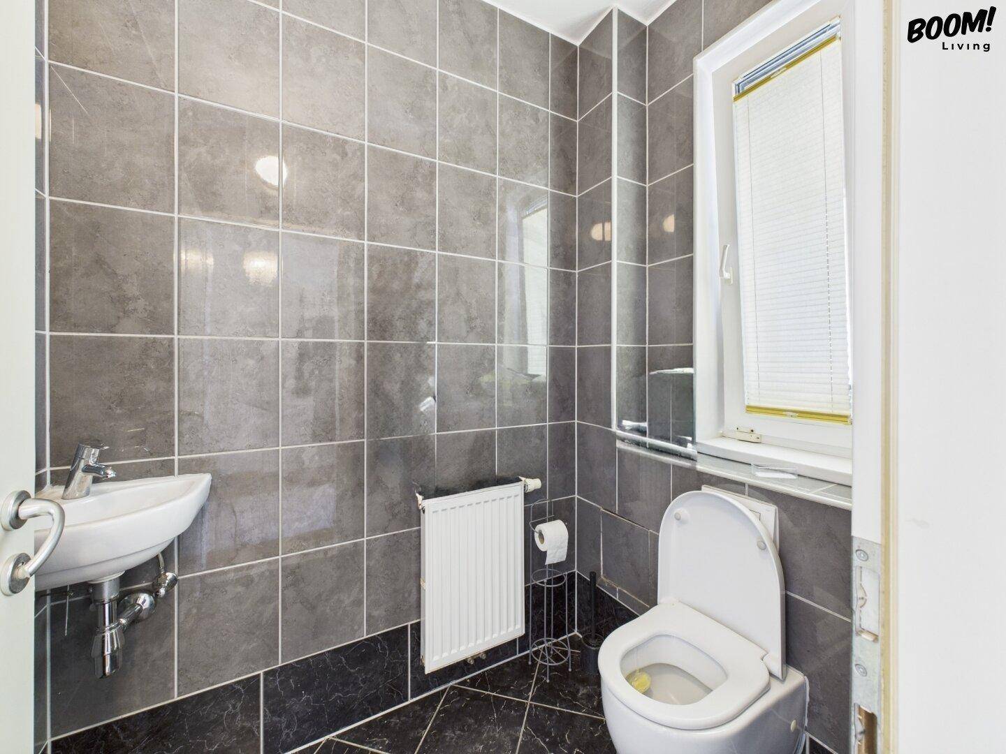 Kleines Gäste-WC mit grauen Fliesen, wandhängendem WC und kleinem Waschbecken.