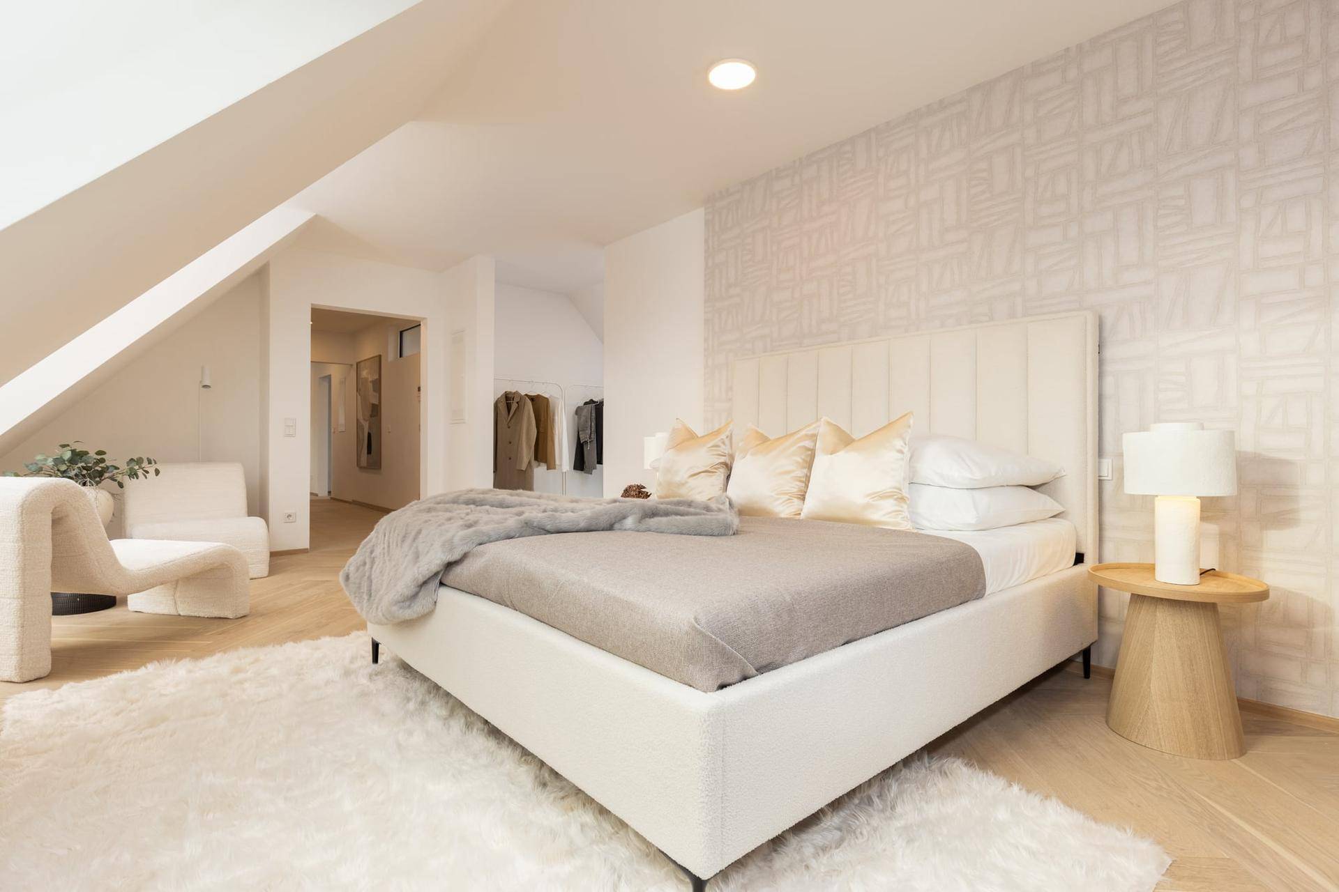 Elegantes Schlafzimmer mit gepolstertem Bett, Holzboden und Zugang zu einem Ankleidebereich.