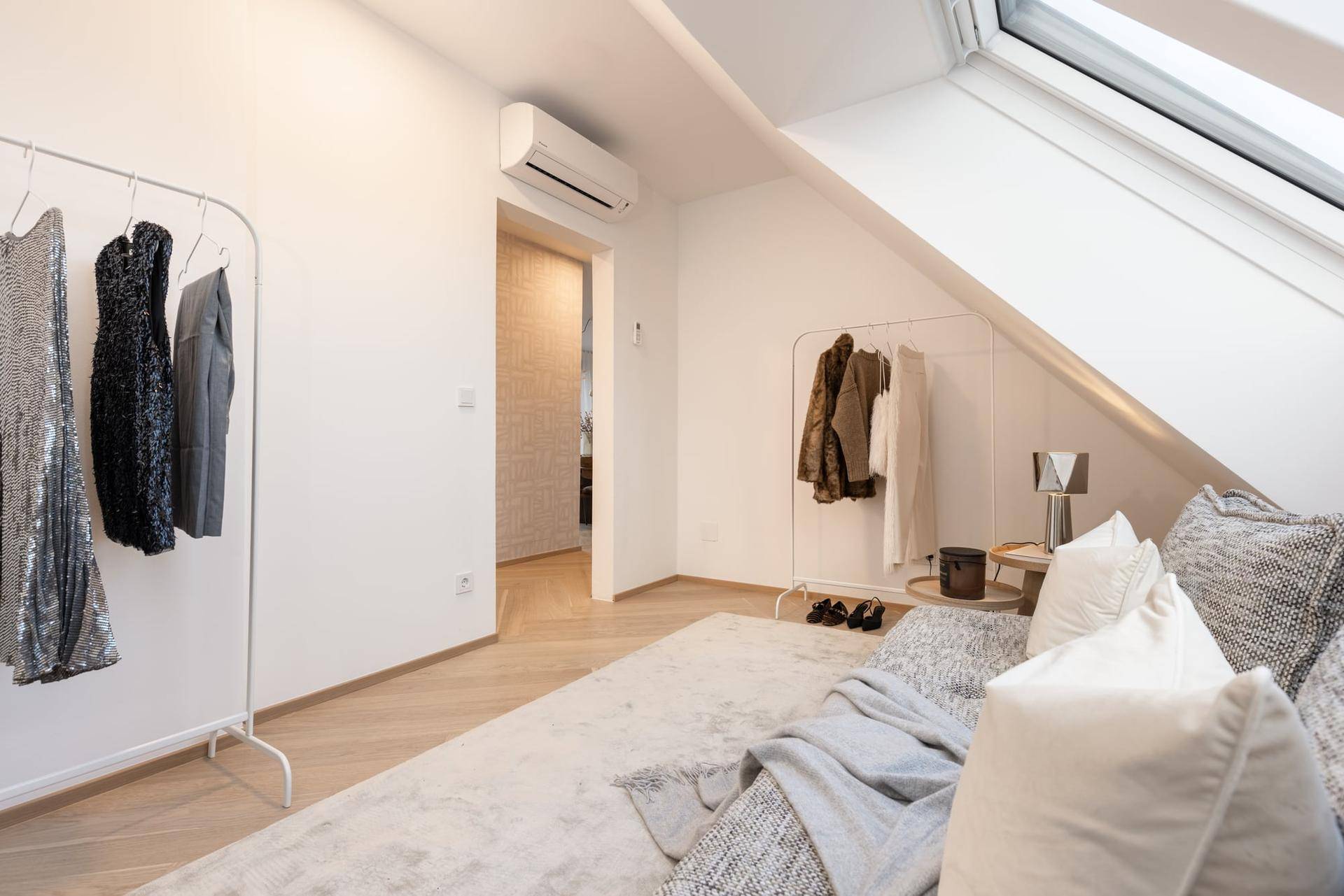 Heller Raum mit Kleiderständern, bequemer Sitzgelegenheit und viel Tageslicht durch Dachfenster.